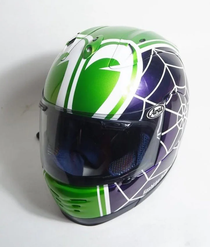 A green and black full-face motorcycle helmet with white and purple accents, featuring a web-like design and a tinted visor.