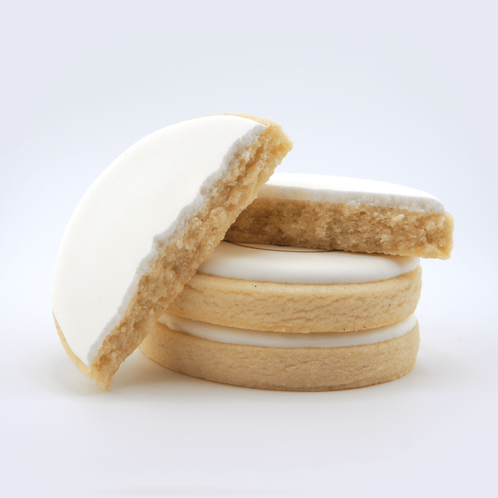 Stacked sugar cookies with white icing, one broken in half showing the inside, on a white background.