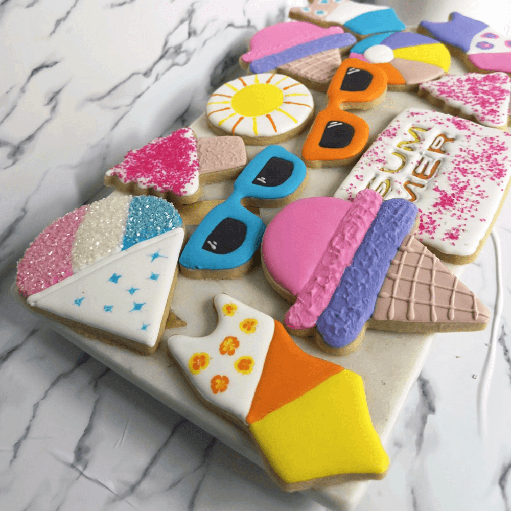 Colorful decorated cookies on a white marble surface, including ice cream cones, sunglasses, a sun, hearts, and a birthday message.