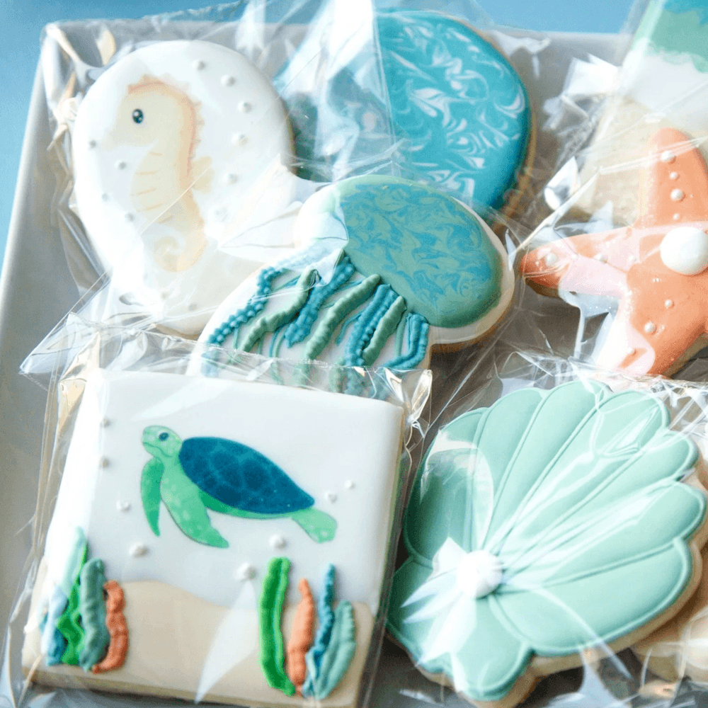 Assorted decorated cookies with ocean theme, including a seahorse, turtle, seashell, and seaweed designs, wrapped in clear plastic.