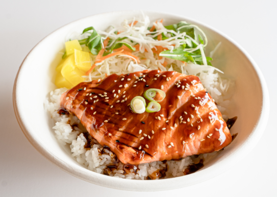 Bowl of rice topped with glazed salmon, garnished with green onion slices, served with shredded cabbage and pineapple chunks.