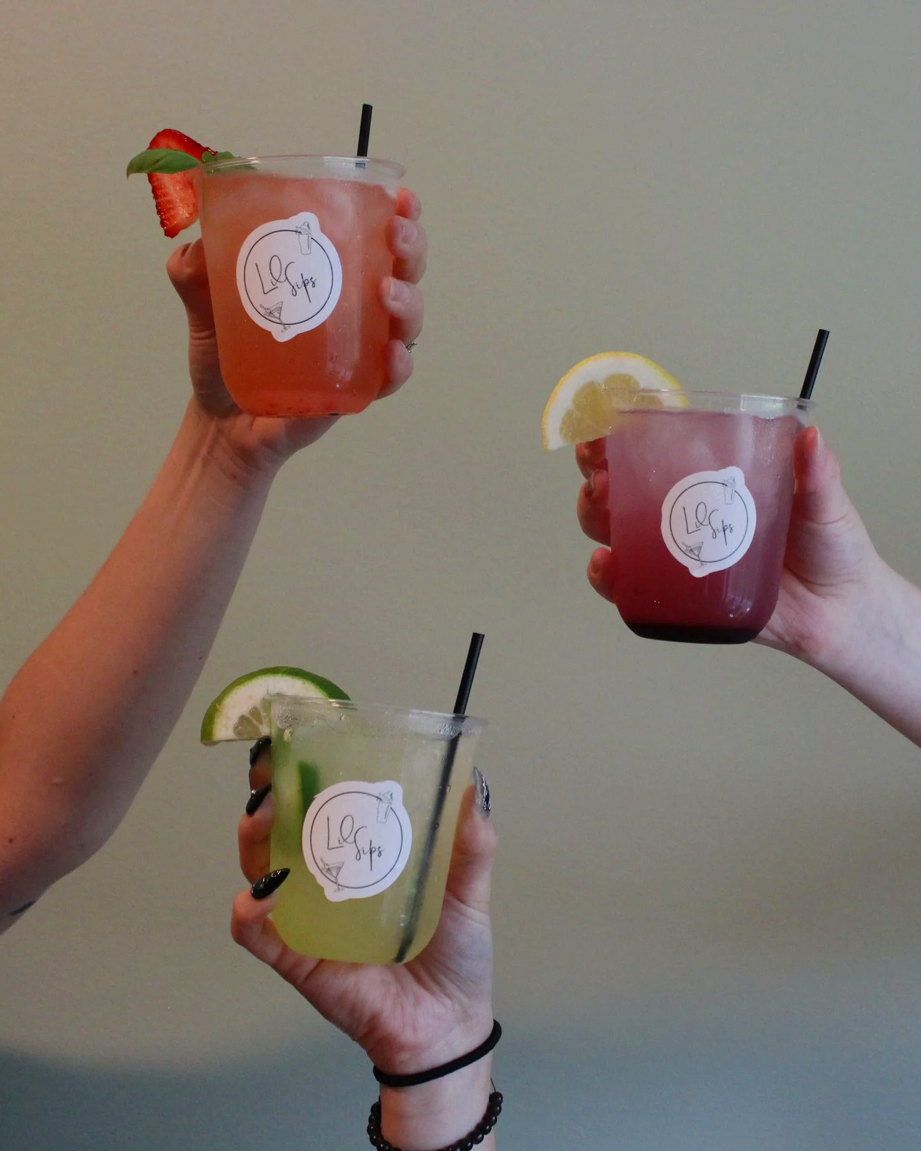 Three people holding colorful drinks with citrus slices and straw, with a plain background.