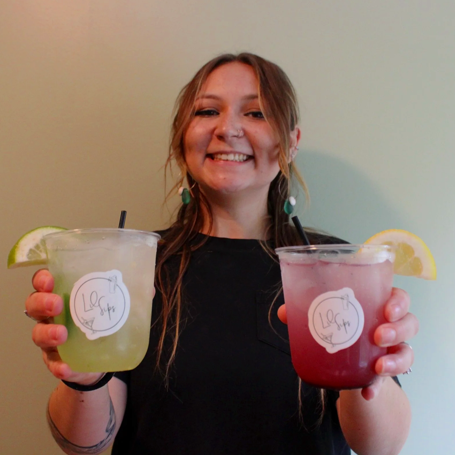 A smiling woman holding two large colorful drinks with lemon and lime slices, each with a label reading 'LilSips'.
