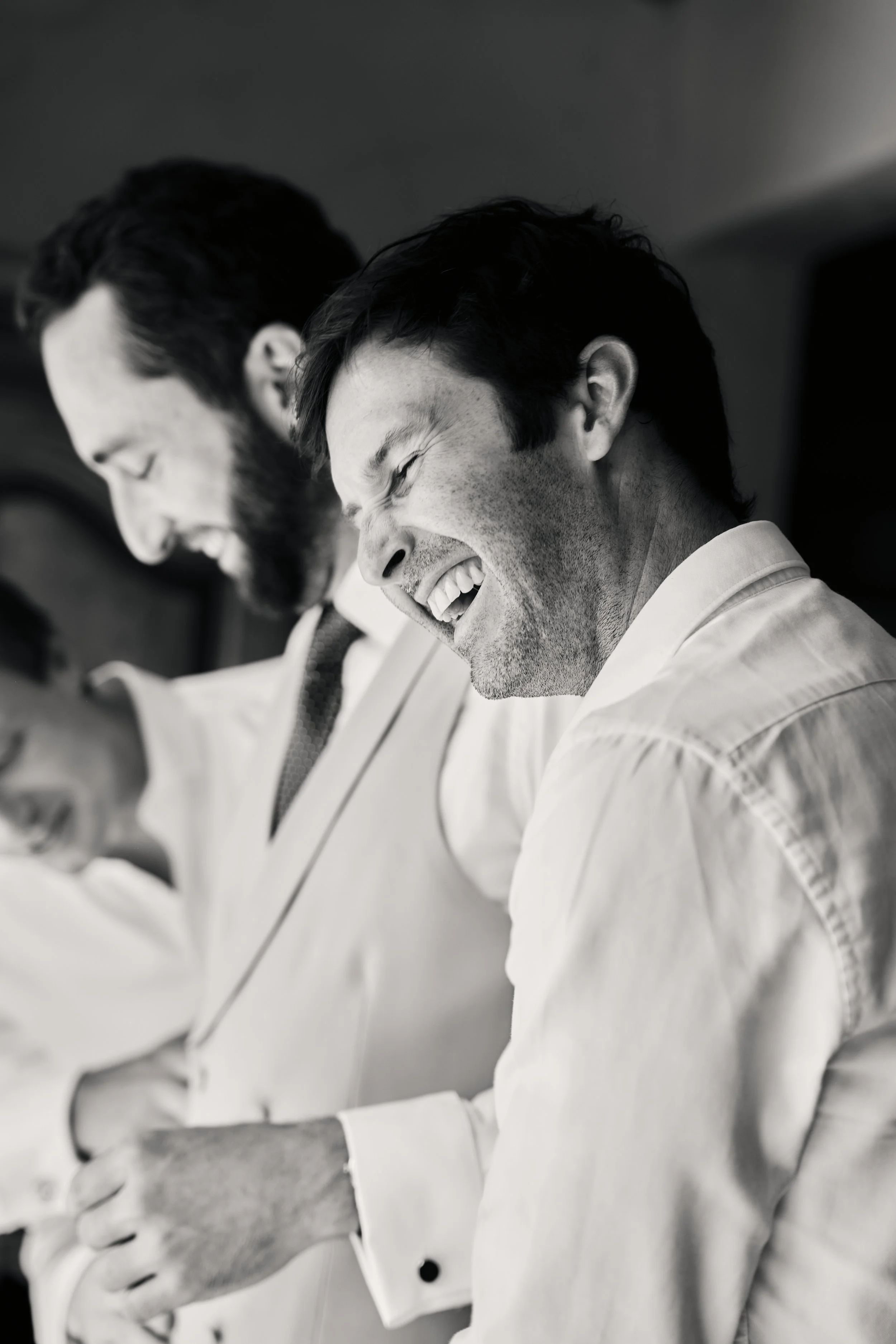 Two men in business attire sitting at a table, both smiling and laughing, in a professional setting.
