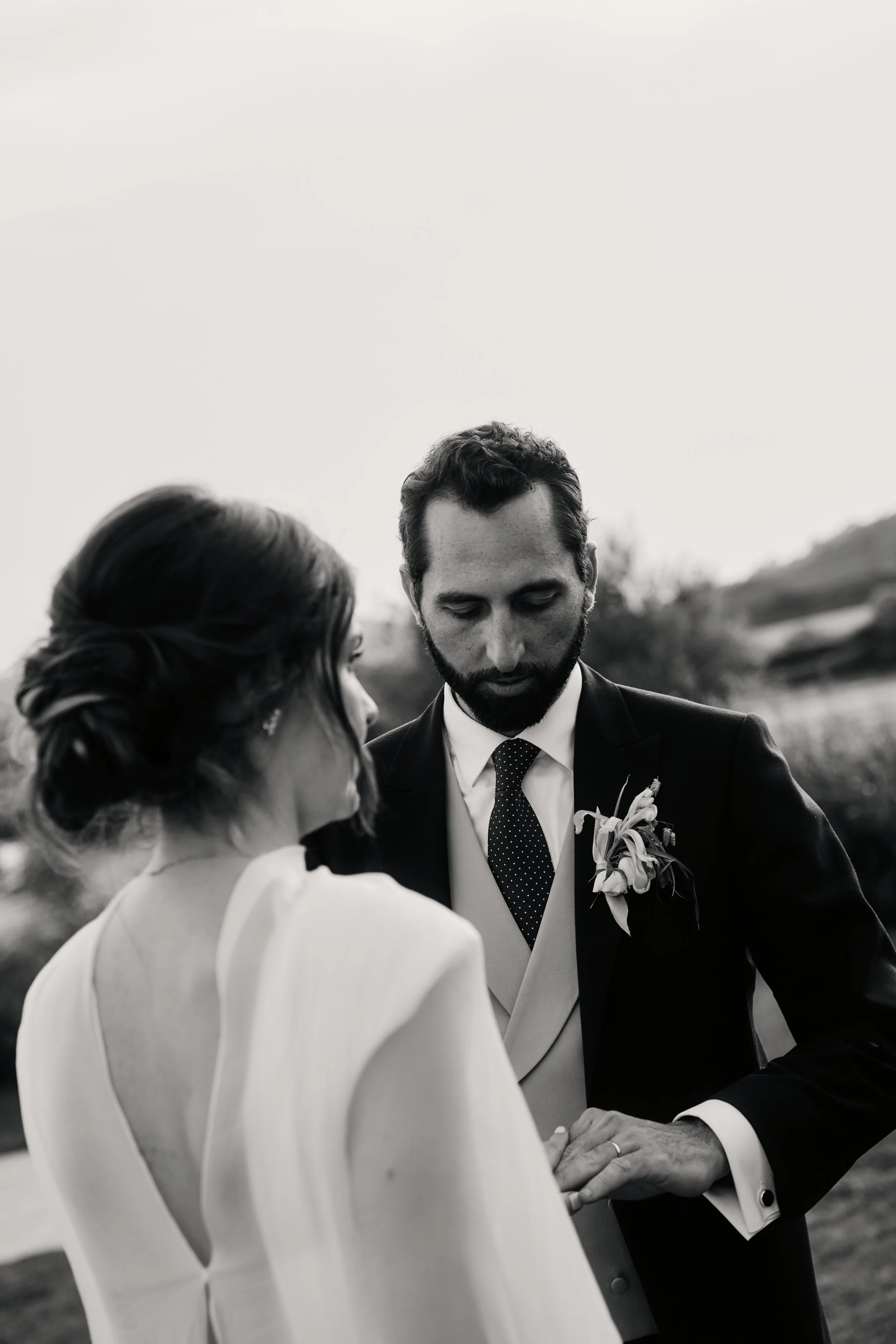Black and white photo of a man and woman holding hands during a wedding ceremony outdoors.