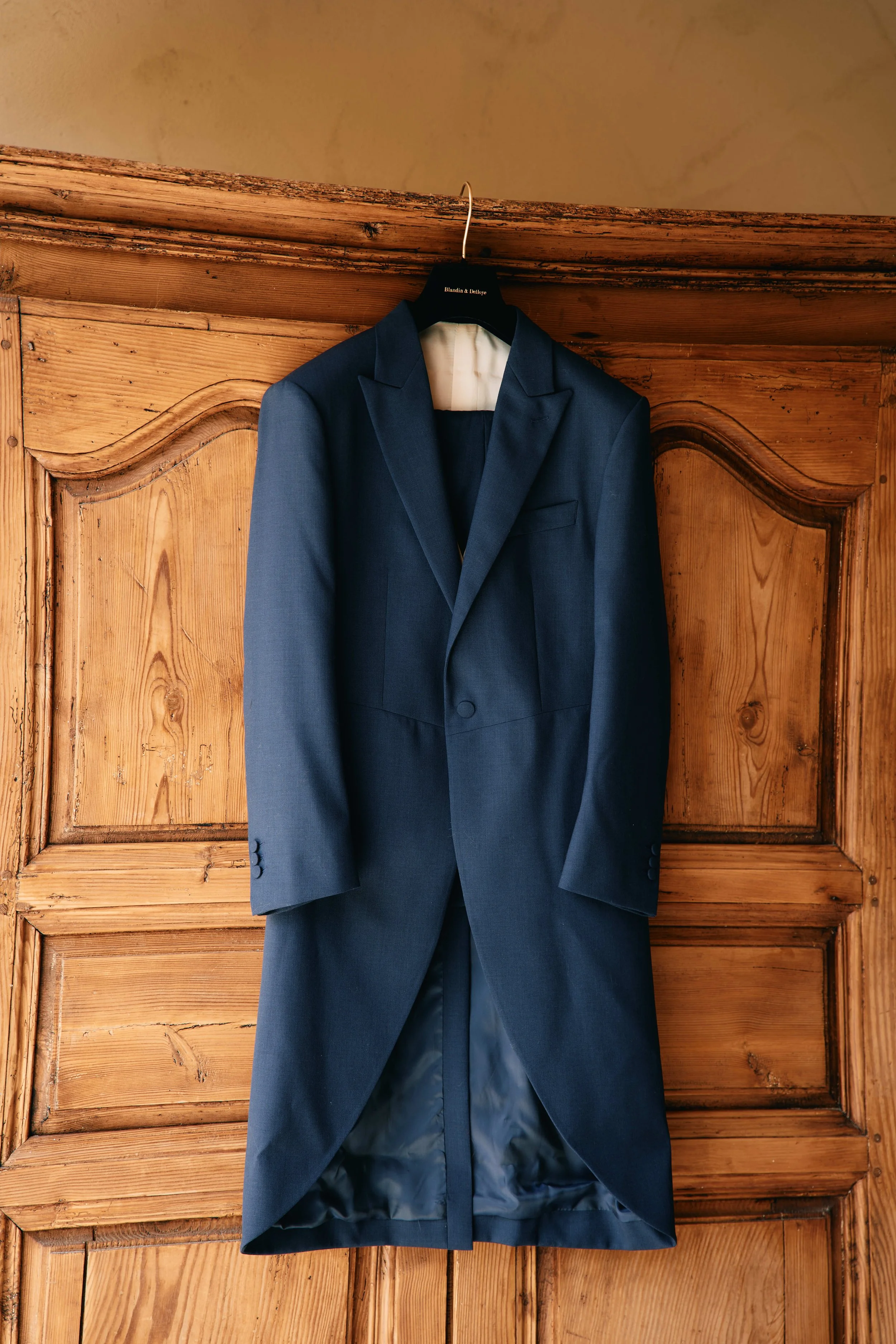 A navy blue suit jacket hanging on a hanger attached to a wooden wardrobe.
