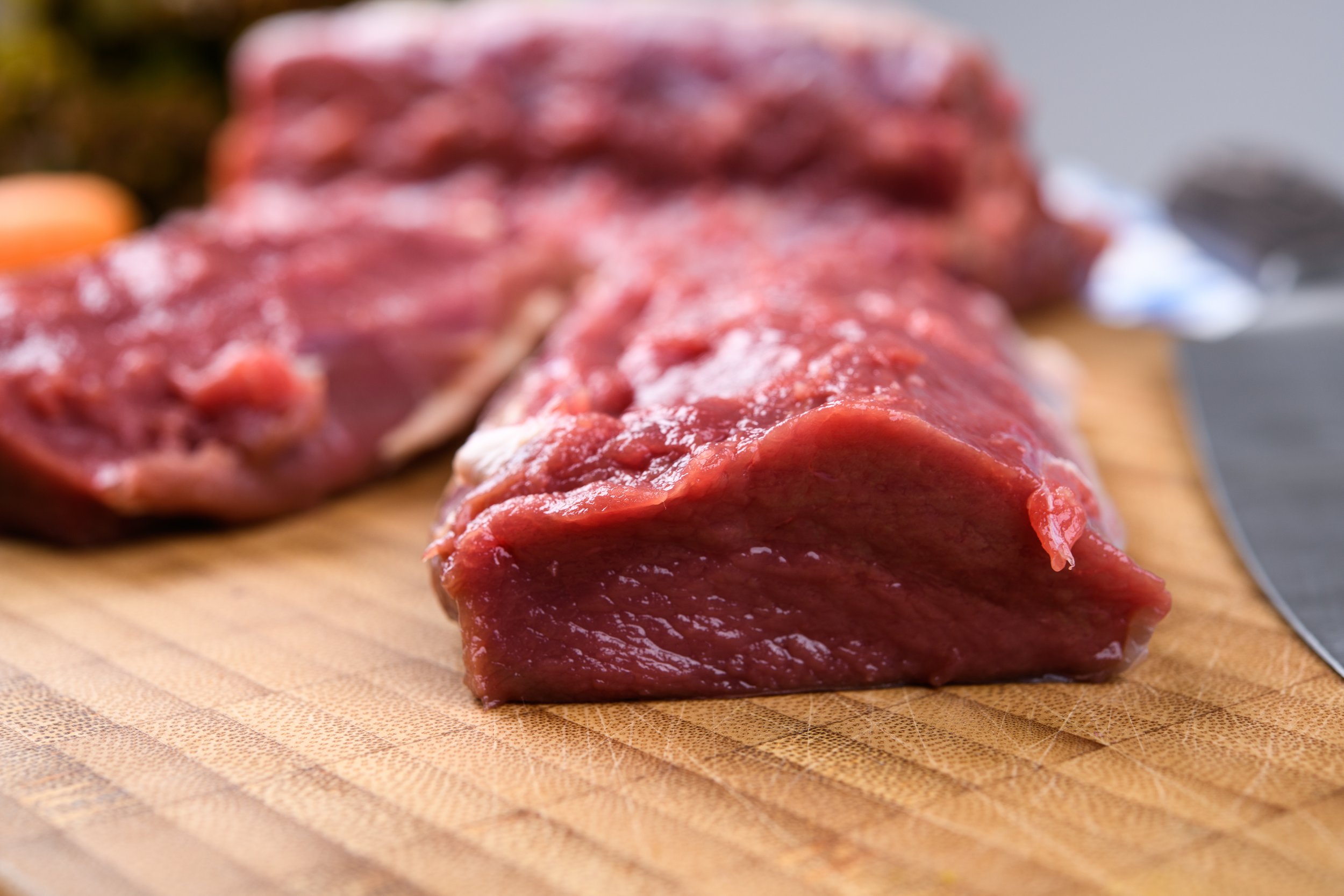 Close-up of raw red meat on a wooden cutting board.
