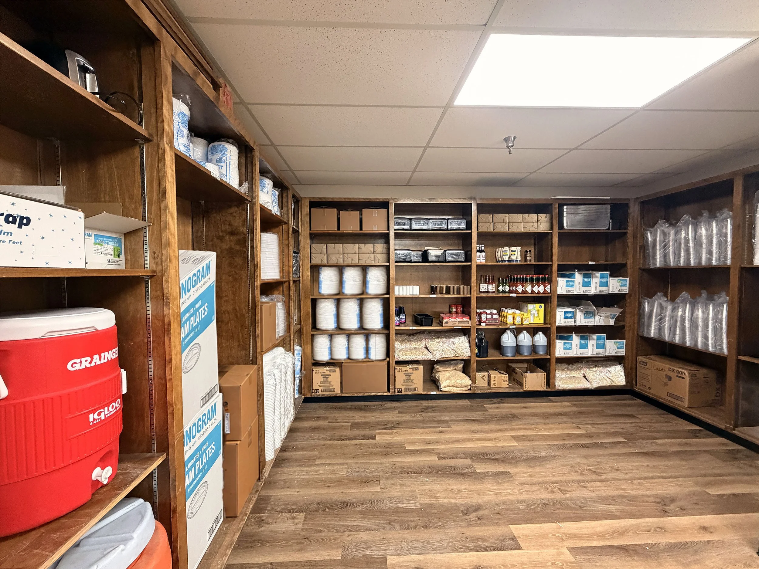 Shelving unit with paper towels, boxes, chemicals, and supplies in a storage room with wood flooring.