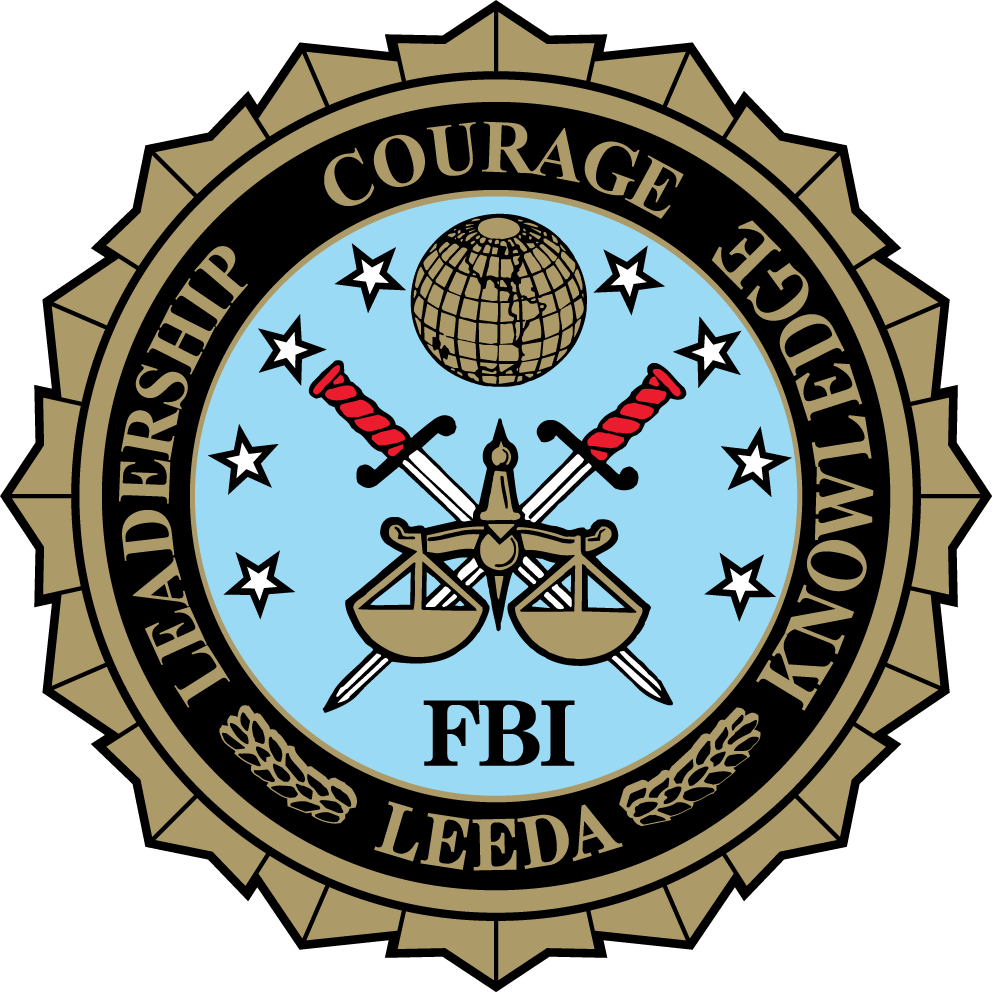 FBI LEEDA badge with a light blue background, featuring two crossed knives with red handles, a pair of scales, a globe, and surrounded by the words 'Leadership', 'Courage', 'Service', and 'Knowledge'.