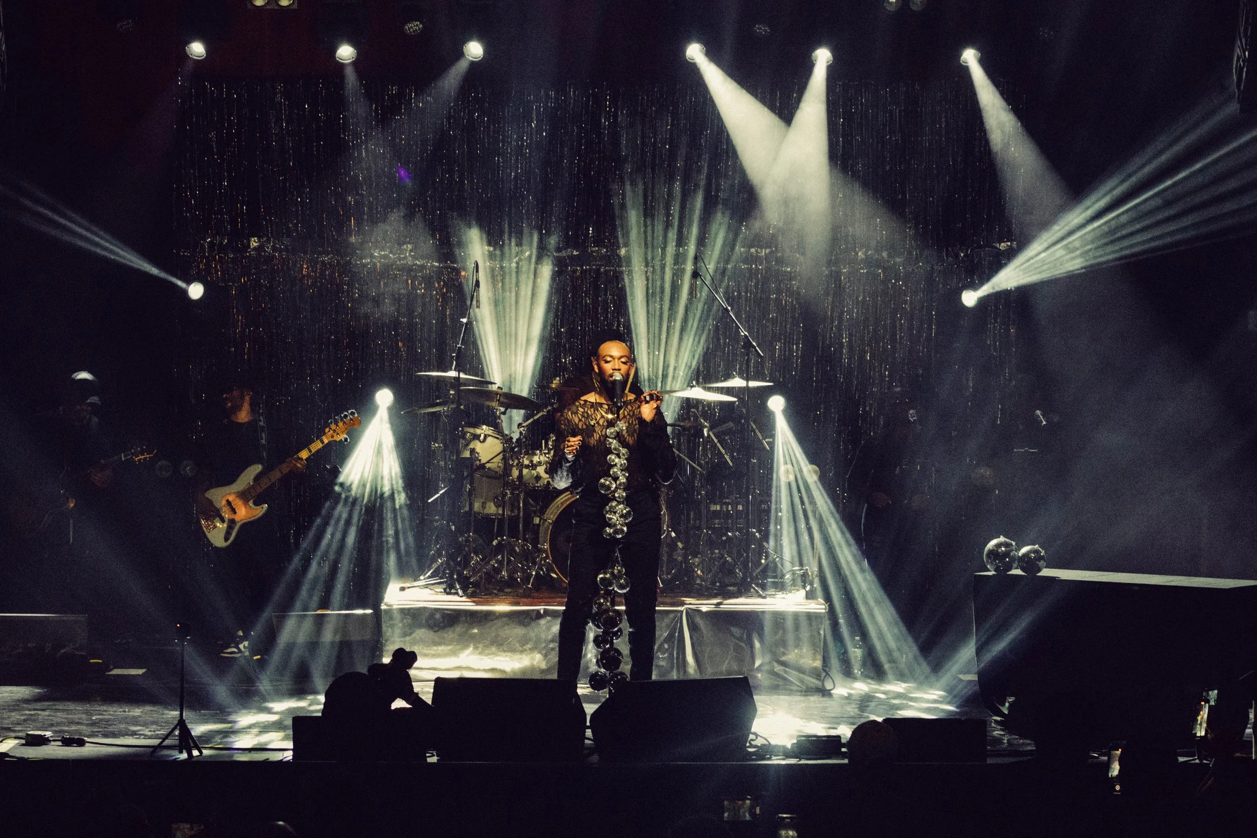 Dexter Jordan the  singer performing on stage with band members and vibrant stage lighting, including spotlights and sparkling background.