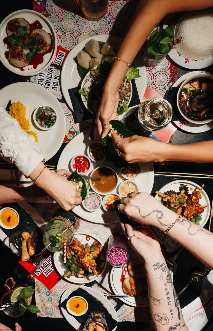 People sharing a meal with various Asian dishes and drinks on a decorated table.