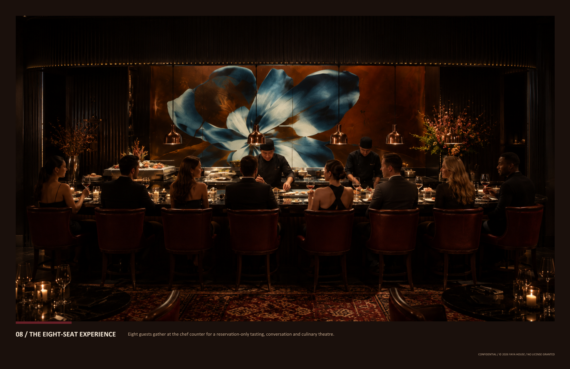 Eight people seated around a rectangular dining table in a dimly lit restaurant, with chefs preparing food at a counter behind them, and a large abstract flower mural on the wall.
