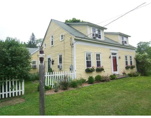 Yellow house with white trim, front garden with flower boxes, white picket fence, and a lamp post in the yard.