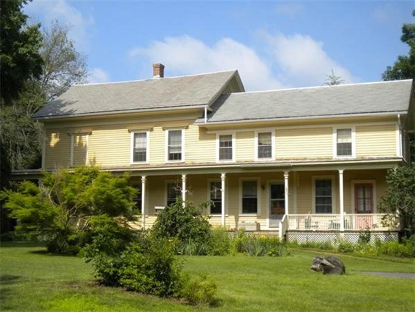 Yellow two-story house with a front porch and lush green lawn.