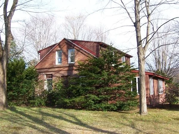 A brick house with a red roof surrounded by trees and shrubs, with a grassy yard in front.