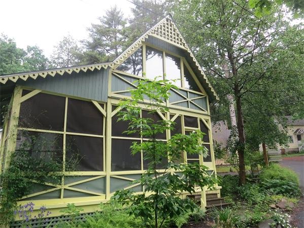 Green house with screened porch and decorative trim, surrounded by trees and plants.