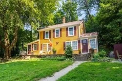Yellow and purple two-story house with outdoor staircase, surrounded by trees and greenery