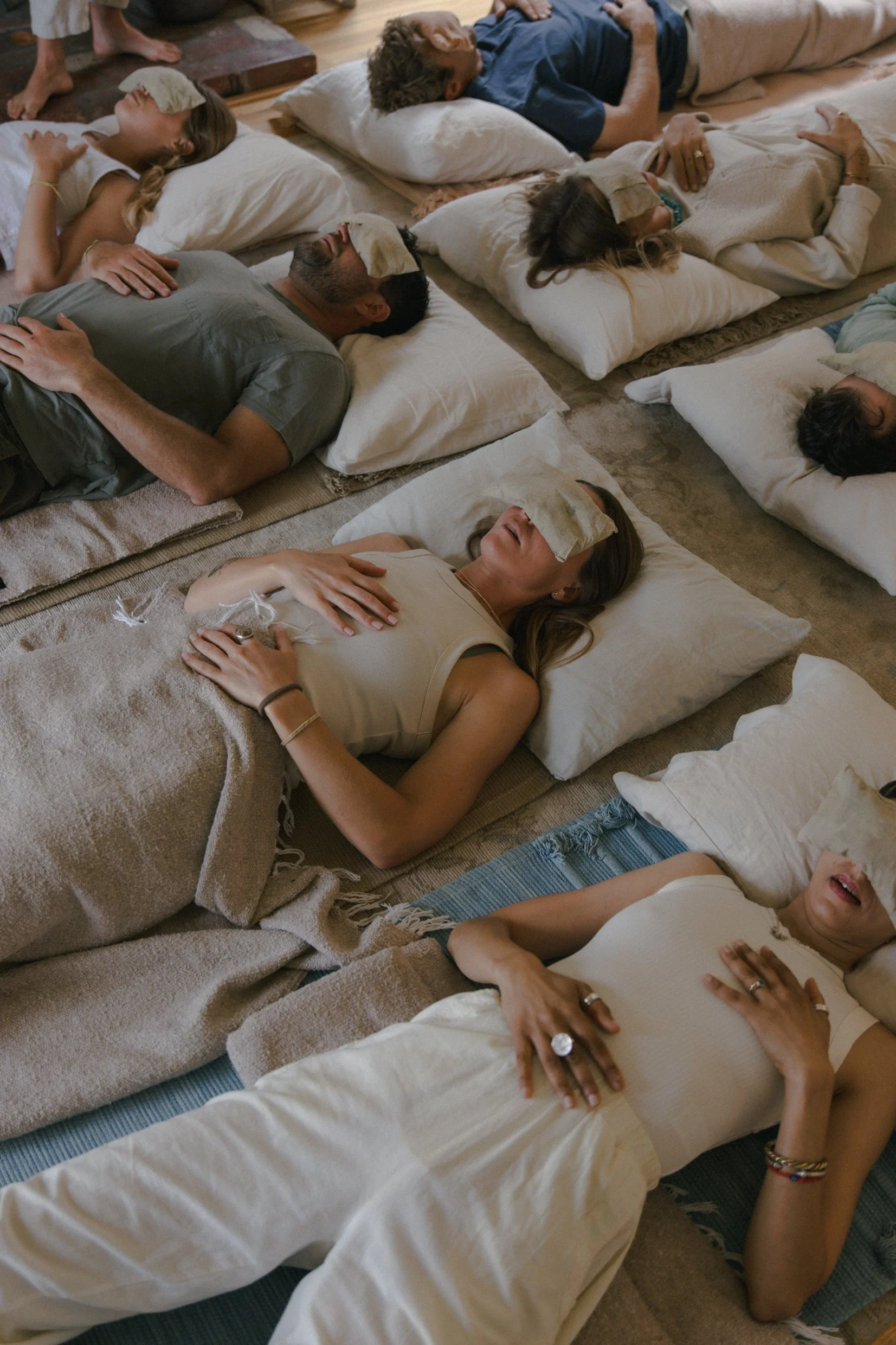 Group of people lying on the floor on pillows with blindfolds, appearing relaxed and meditative.