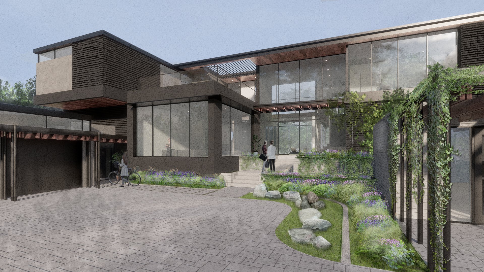 Modern multi-story building with large glass windows and a garden with greenery and flowers in the foreground. Two people are walking and one person is standing near a bicycle.