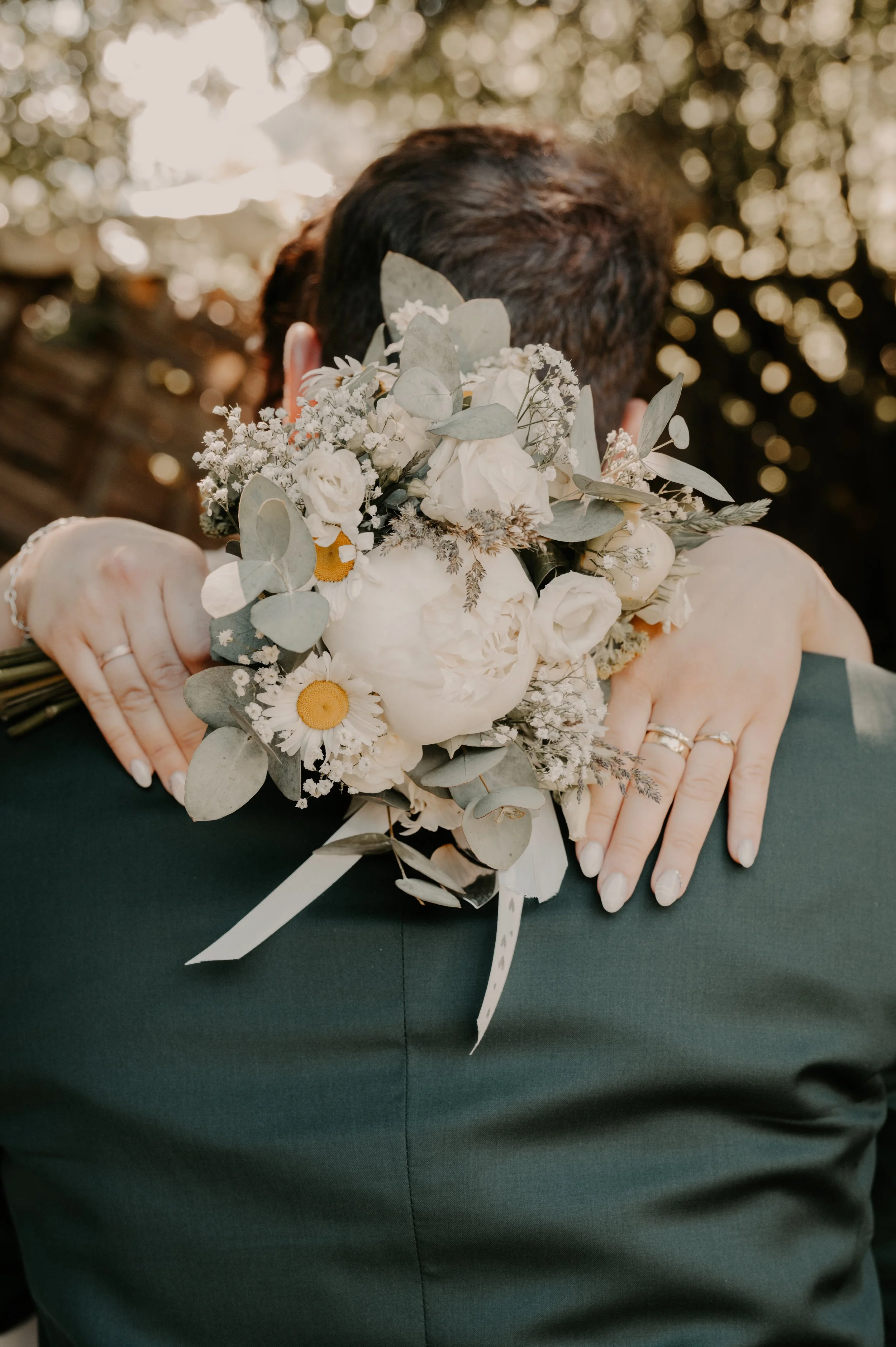 Person holding a bouquet of white flowers with greenery, against a blurred outdoor background.