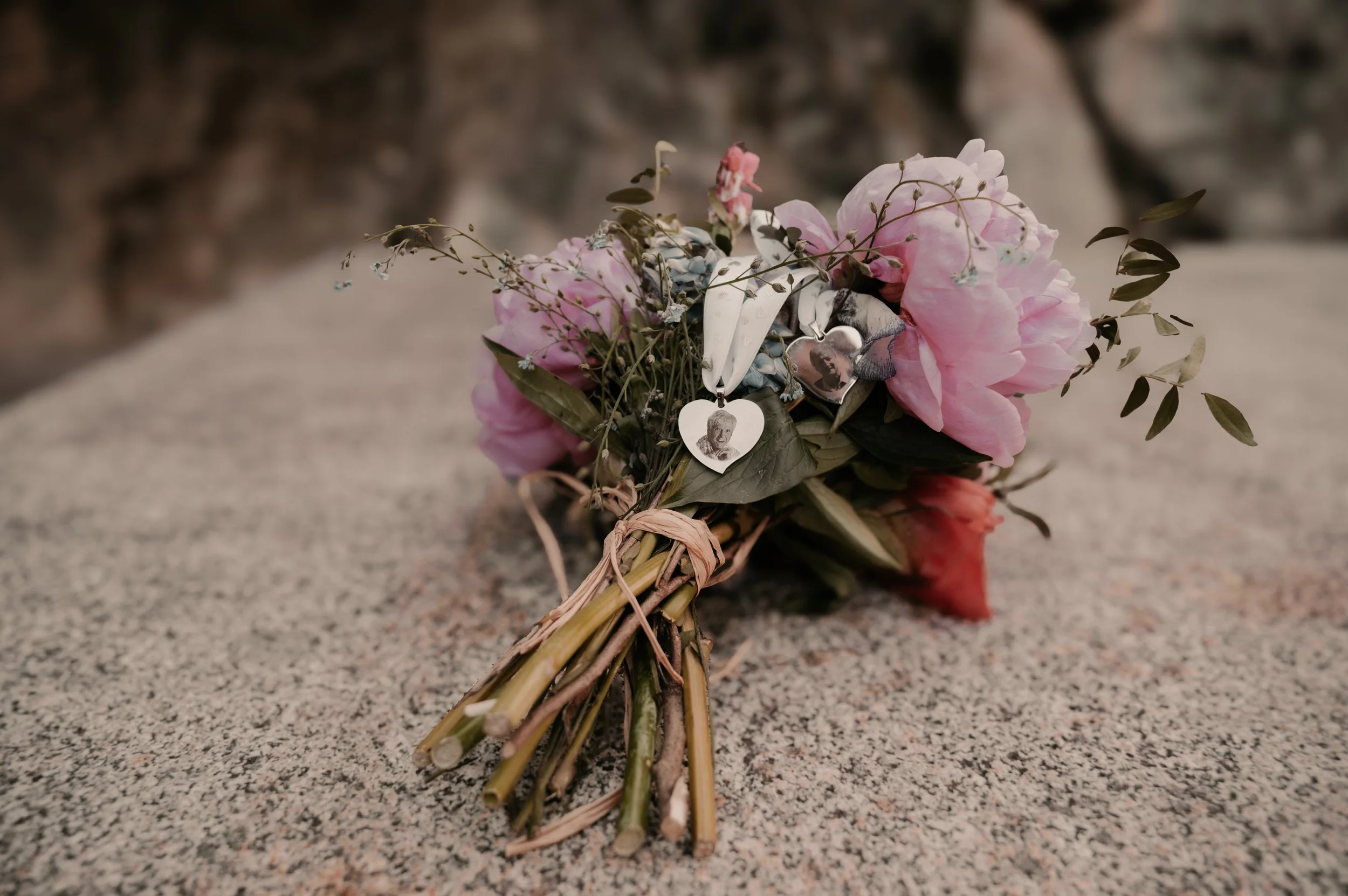 A small bouquet of pink and white flowers with green leaves and dried sprigs, decorated with vintage black and white photographs, lying on a speckled gray surface.