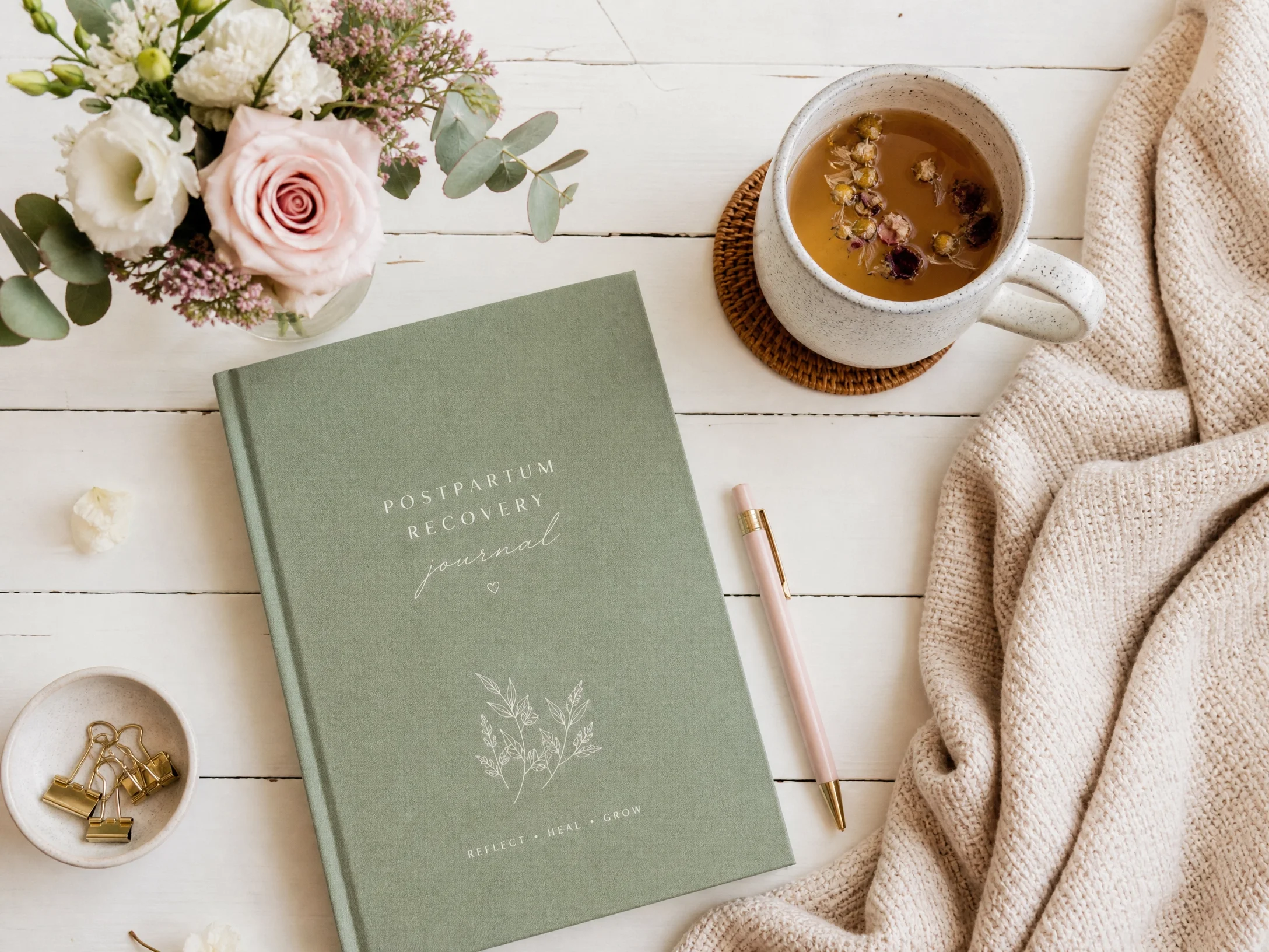 A flat lay of a cozy workspace with a bouquet of white and pink flowers, a green journal titled "Postpartum Recovery Journal". Core & Pelvic Health: Diastasis recti exercises, pelvic floor recovery, postpartum core strength, pelvic health physio