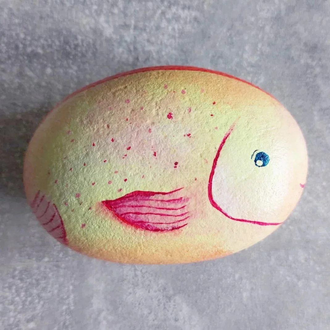 Ein Stein, bemalt als geld-orangener Fisch.