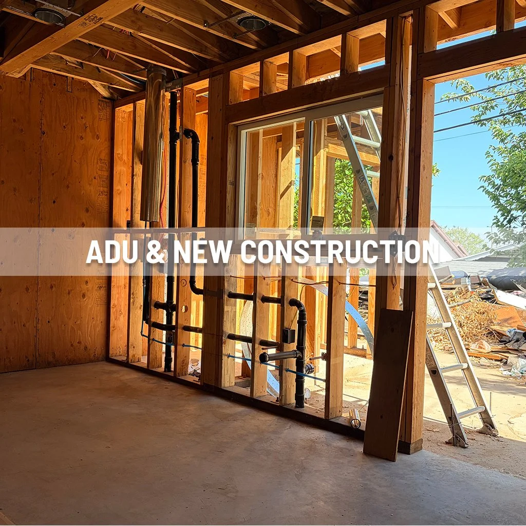 Interior view of a house under construction with wooden framing, plumbing pipes, and a ladder outside the window