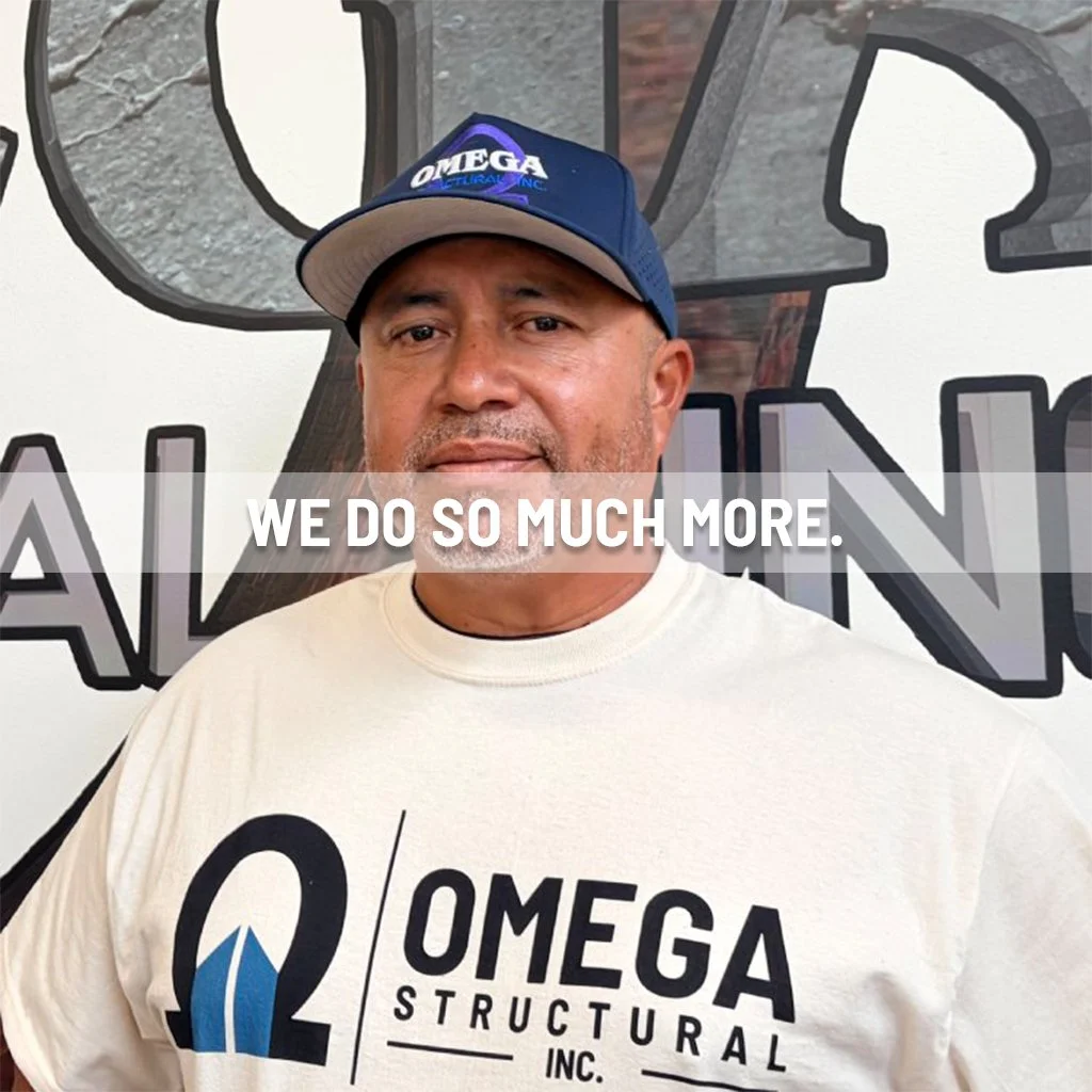 A man wearing a white Omega Structural Inc. T-shirt and a blue Omega Ultra Inc. baseball cap standing in front of a sign. The sign has large stylized letters behind him, possibly part of a larger word or logo, with the prominent text overlaying the image saying "WE DO SO MUCH MORE."