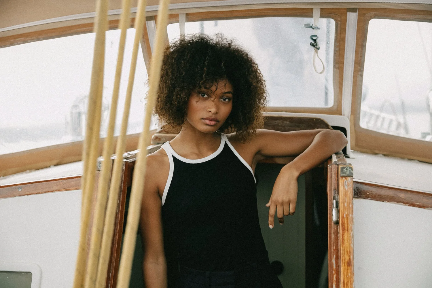 Artlove — Shooting mode d’une femme aux cheveux bouclés portant un haut noir et blanc dans un bateau en bois.