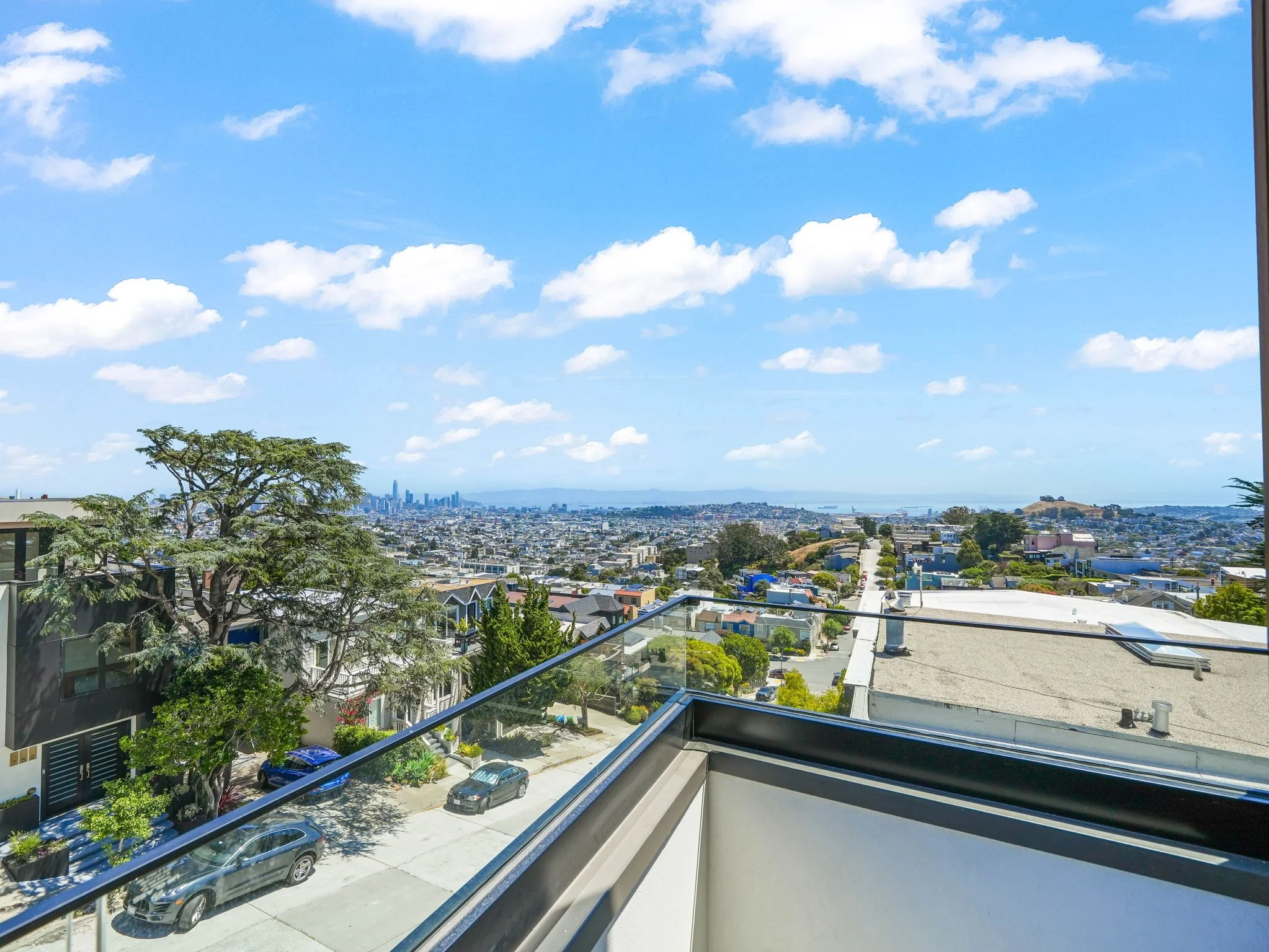 View from a balcony overlooking a cityscape with a skyline in the distance, along with a blue sky and scattered white clouds.