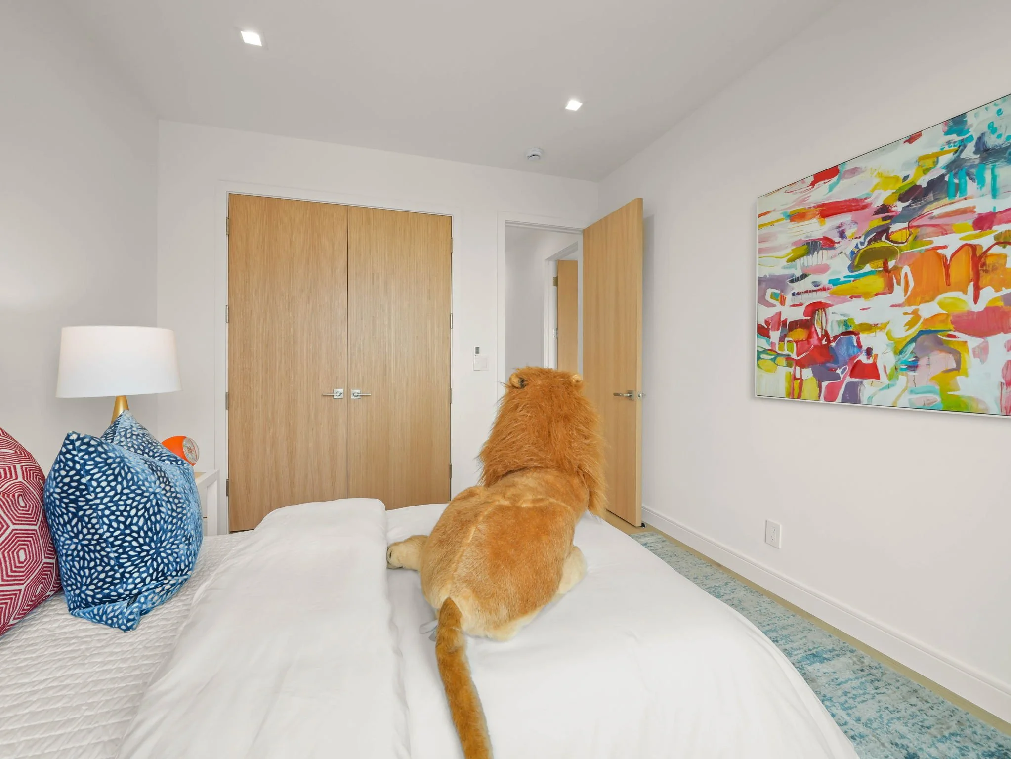 A dog with fluffy orange fur is lying on a bed, facing away from the camera, in a modern bedroom with colorful abstract artwork on the wall.