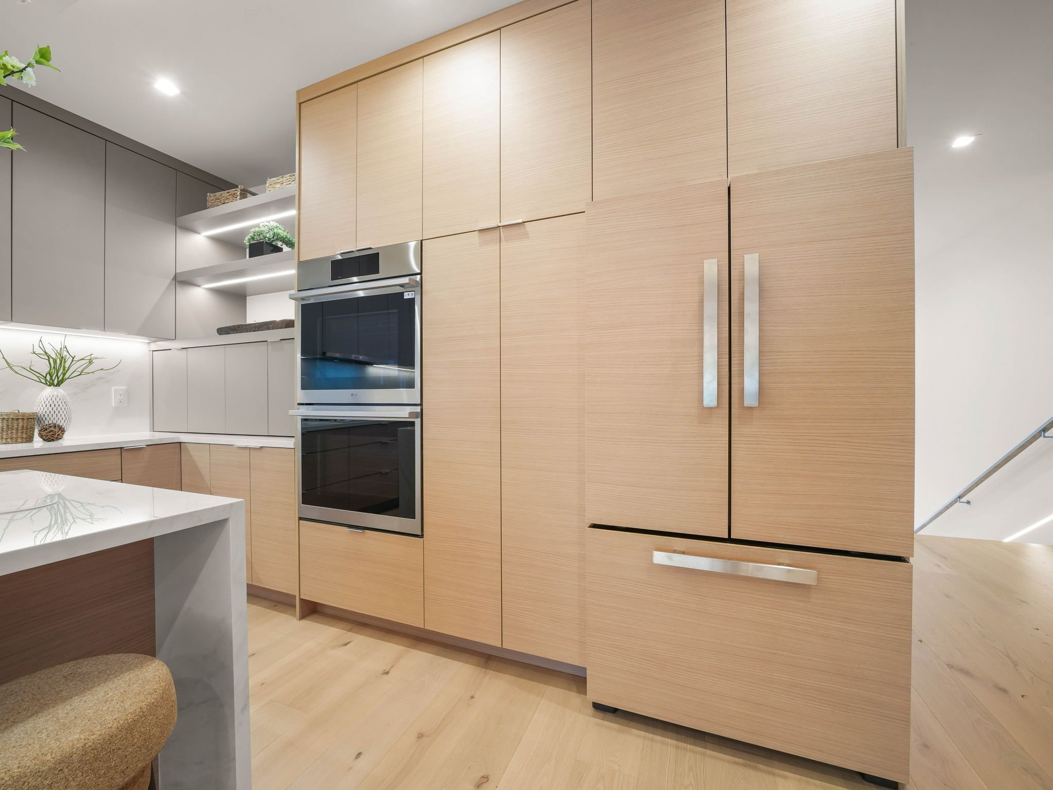 Modern kitchen with light wooden cabinets, stainless steel oven, white countertop, and potted plant on the shelf.