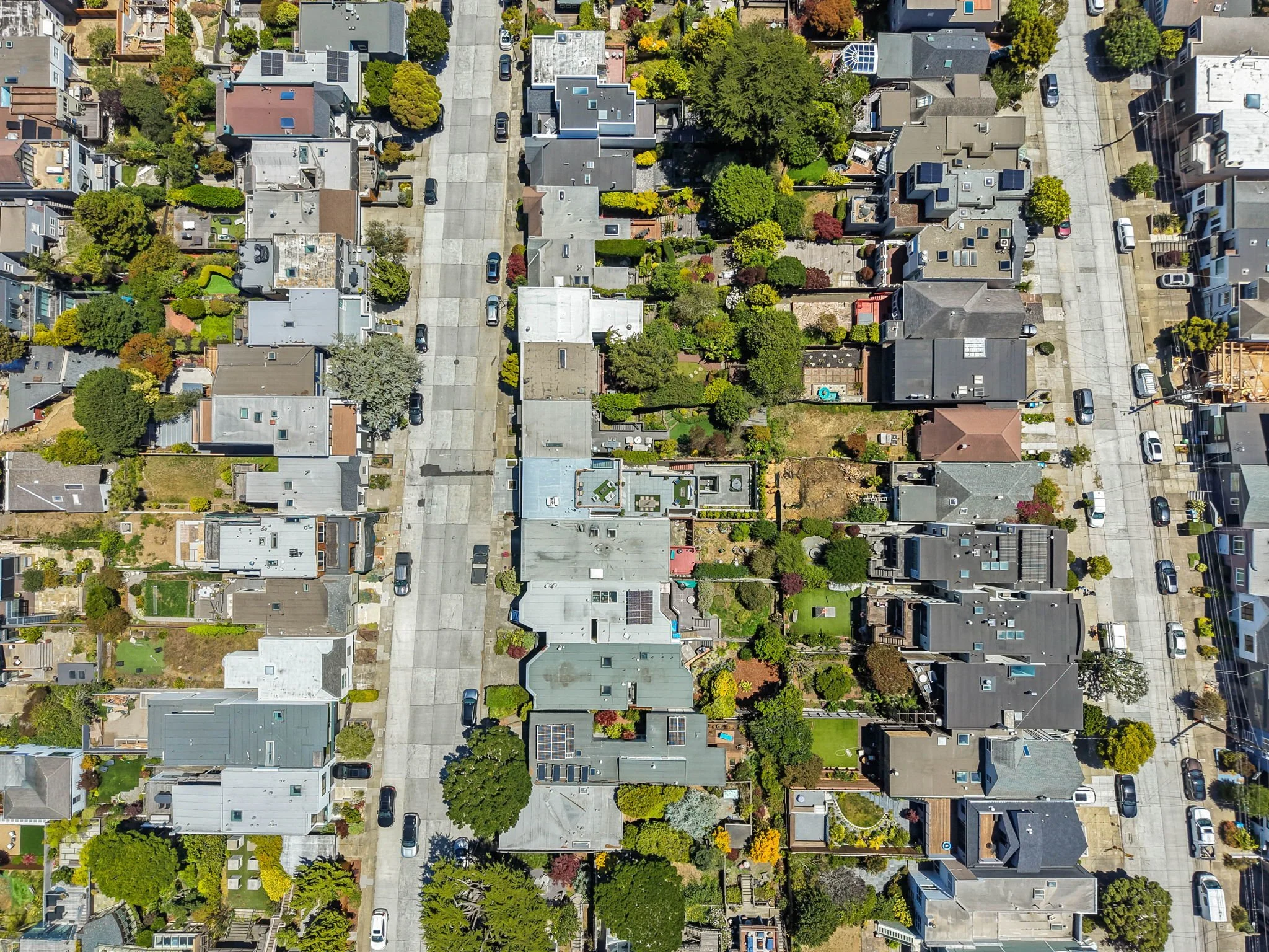 Aerial view of a neighborhood with houses, trees, and parked cars on the streets.