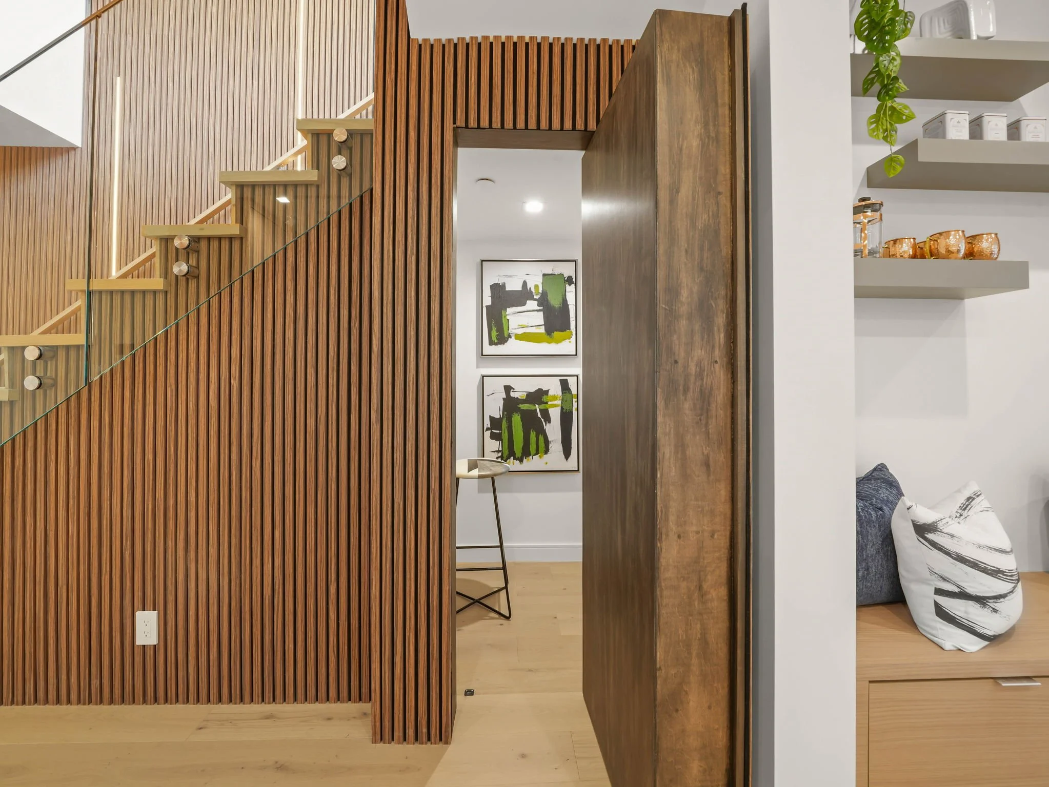Interior of a modern home with wooden slat wall, artwork, bar cart with glasses, and decorative pillows.
