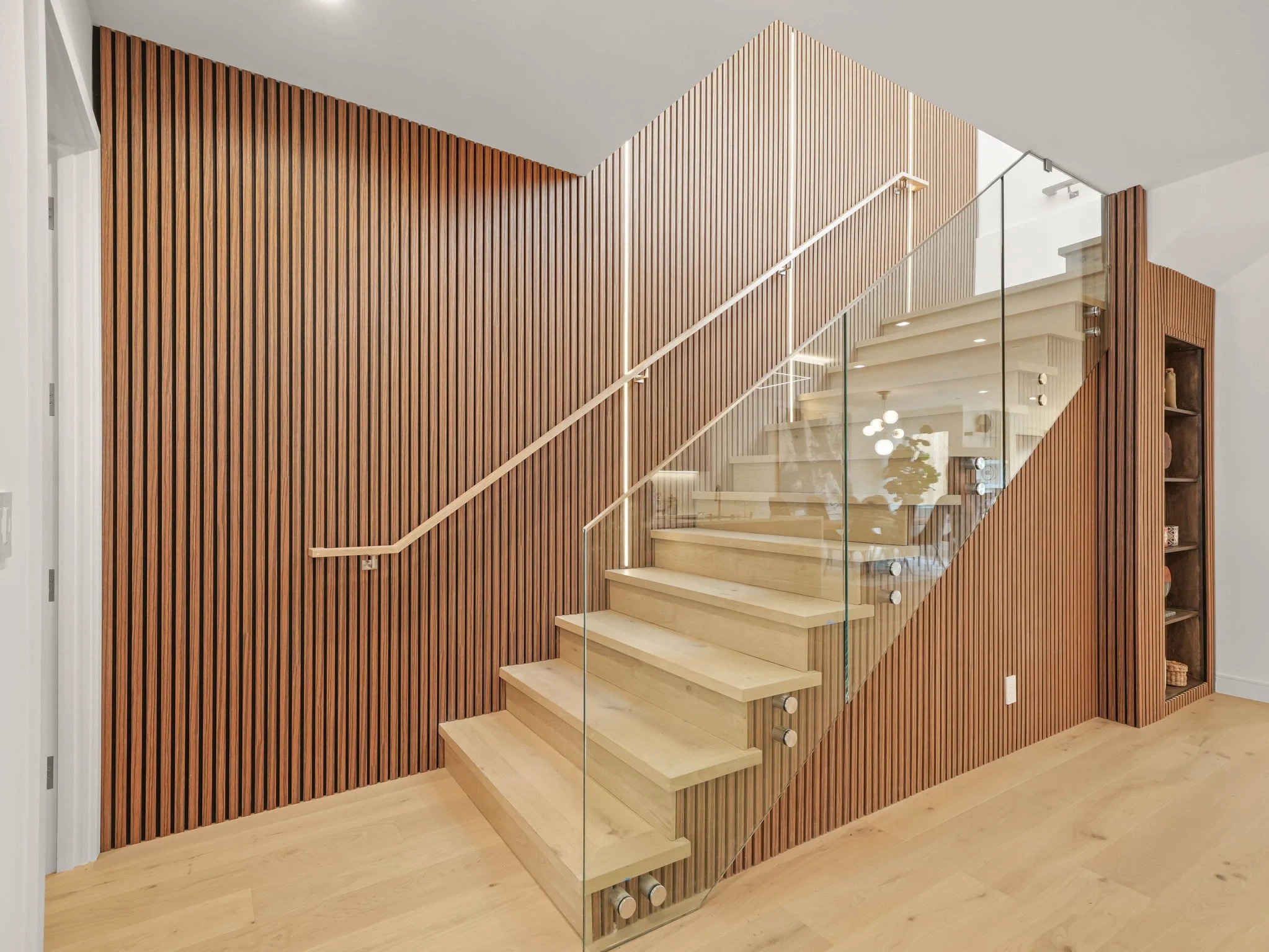 Modern interior with a glass staircase, wooden slat wall, and hardwood flooring.