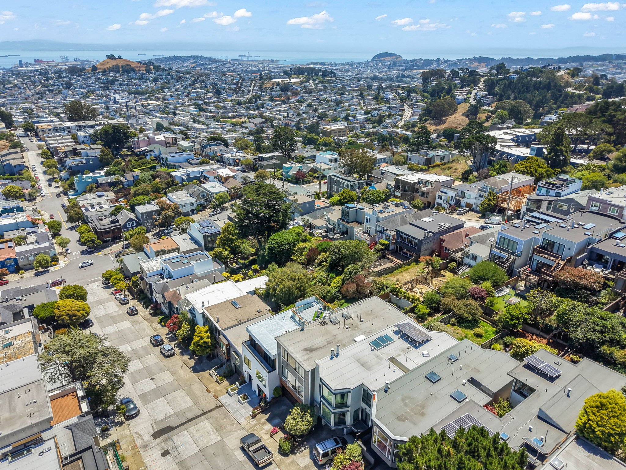 Aerial view of a hillside city with across the bay to water and ships, houses, and greenery.