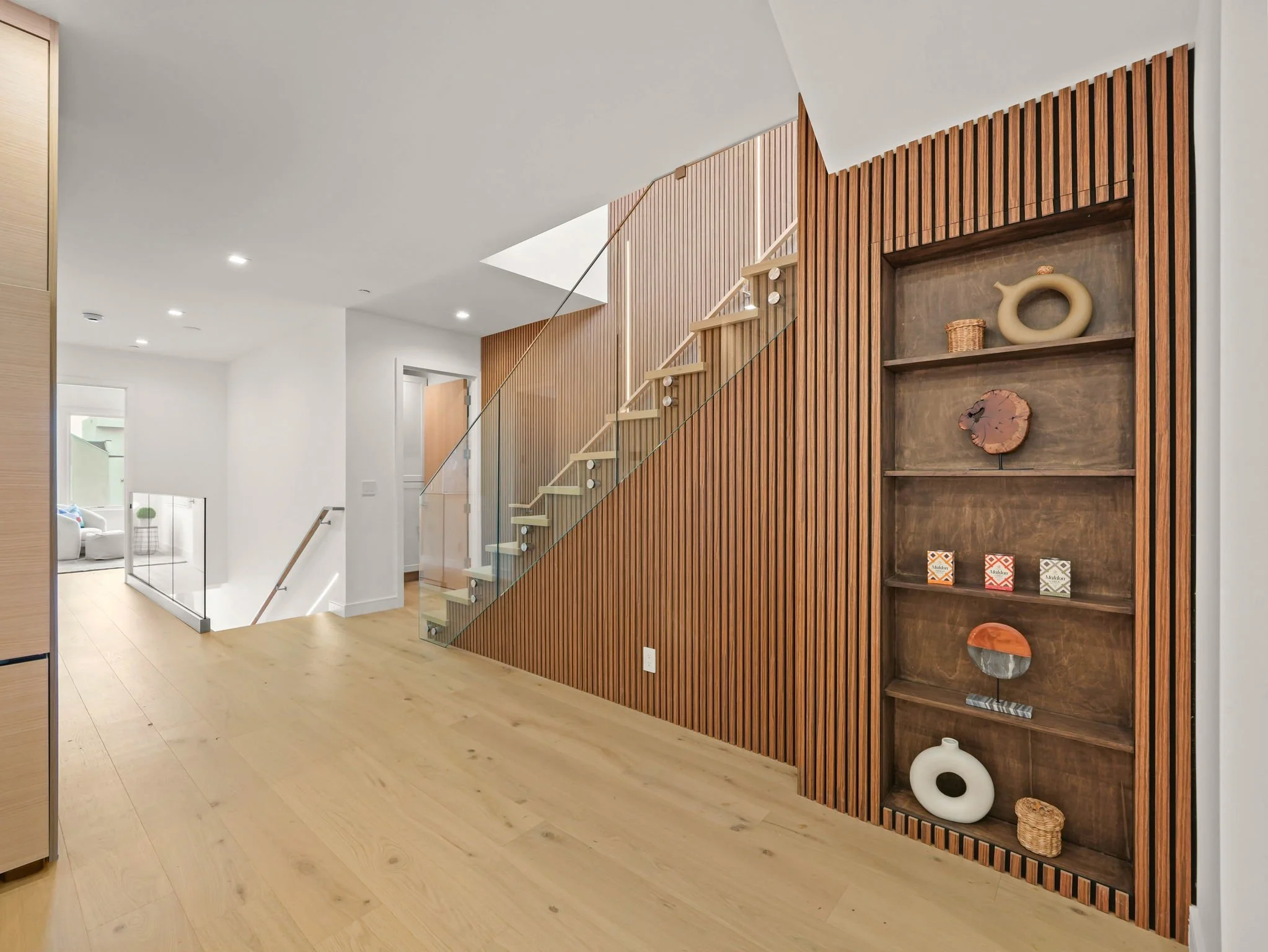 Modern interior with a wooden slat wall, a small staircase with glass railing, and decorative items in built-in shelves.