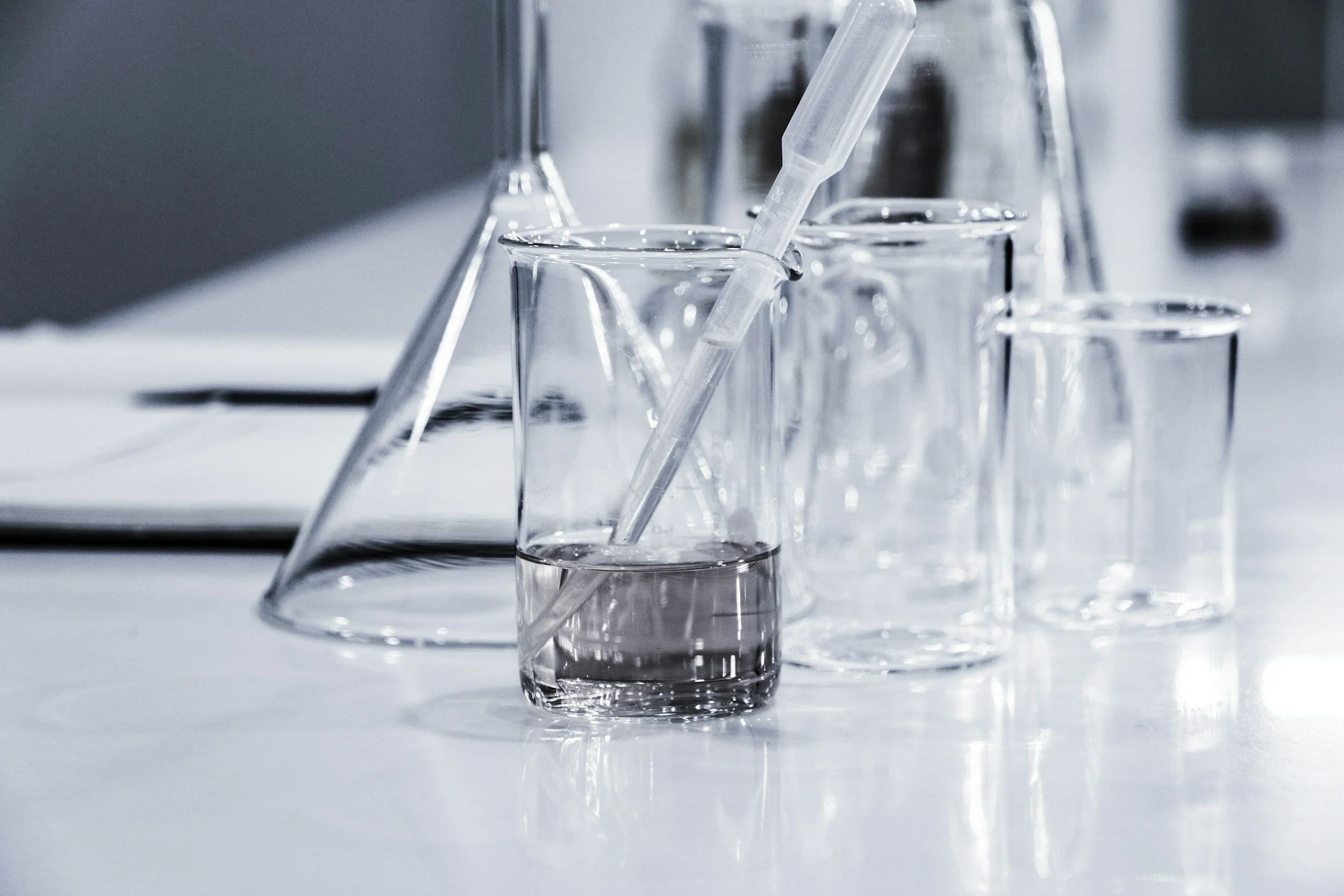 Multiple clear glass laboratory beakers and test tubes with a pipette in a science lab setting.