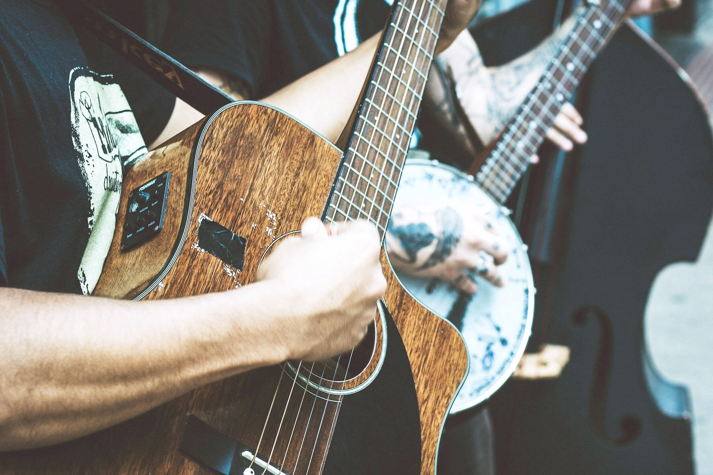 Close-up of two people playing acoustic guitars, their hands and the guitars are in focus, with one person wearing a black shirt and the other in patterned clothing.