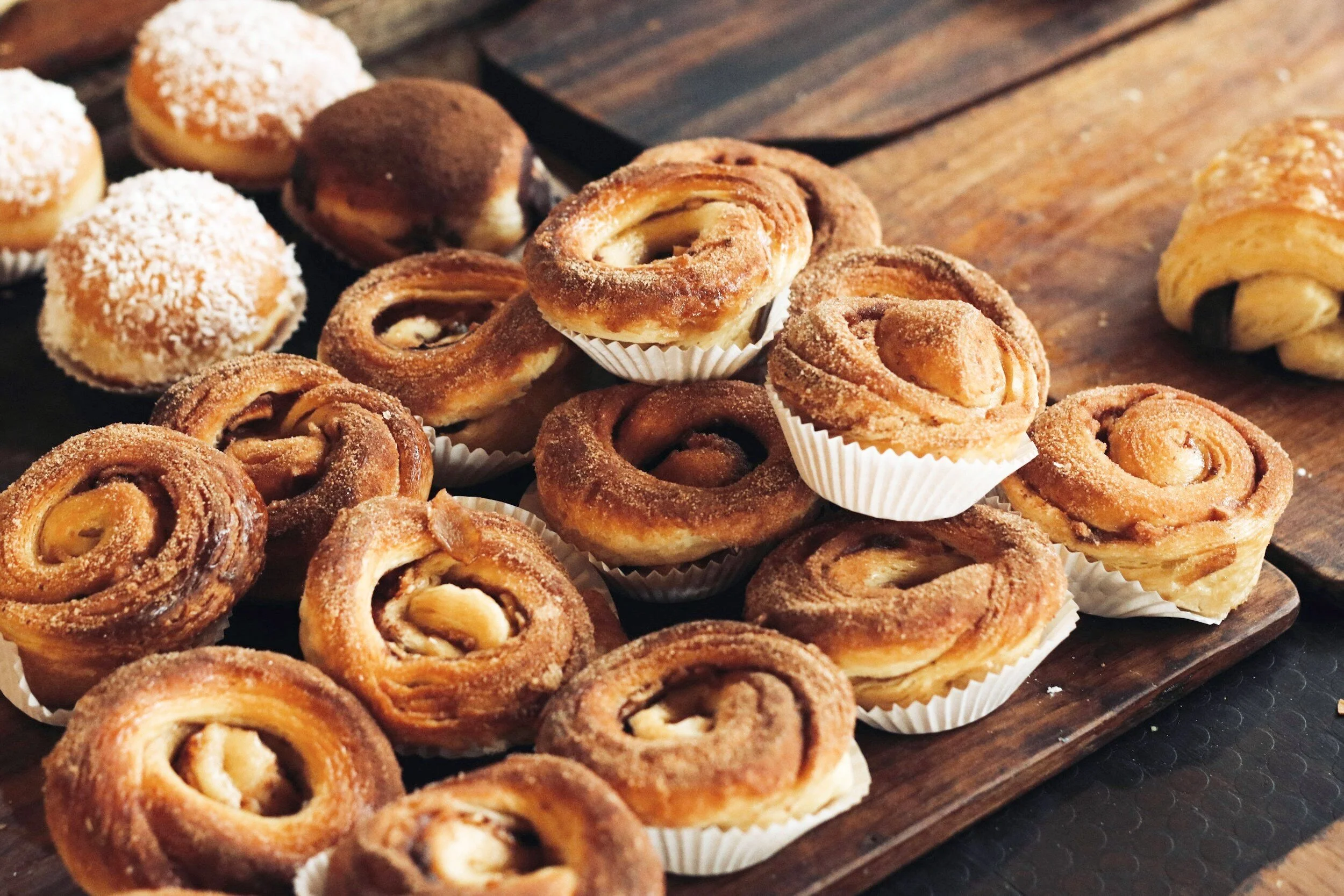 Assorted baked goods, including cinnamon rolls and cream-filled pastries, arranged on a wooden surface.