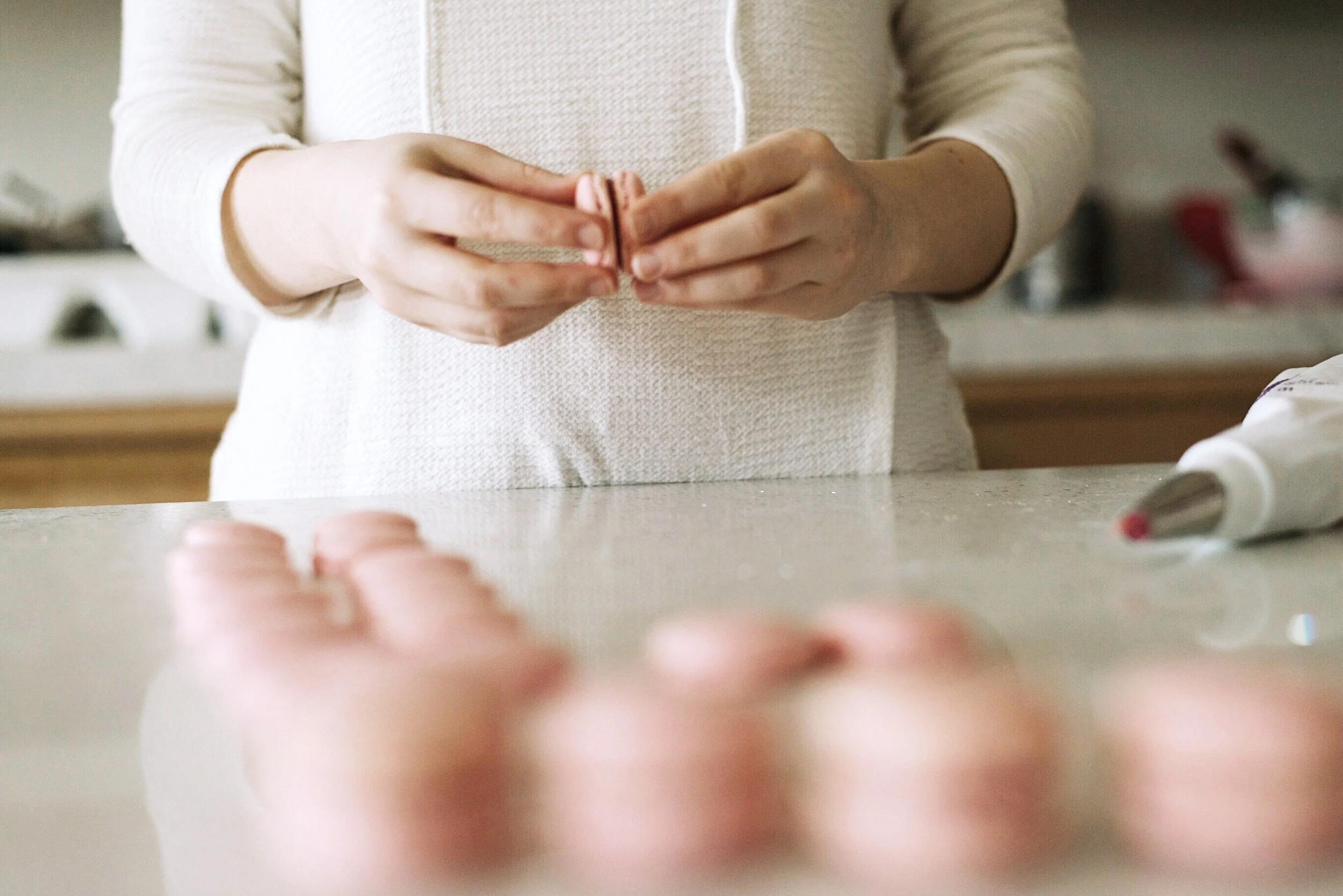 Person wearing a cream-colored sweater holding pink macarons.