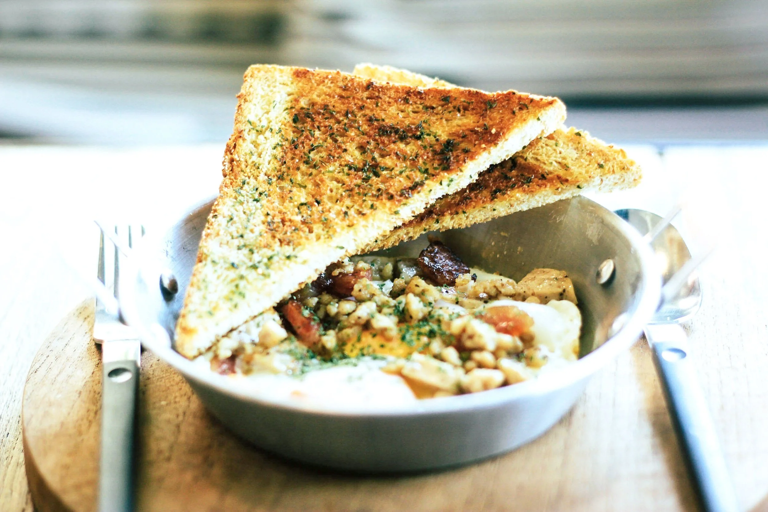 A bowl of food with two slices of toasted bread resting on top, with a mixture of grains, vegetables, and possibly eggs inside the bowl.