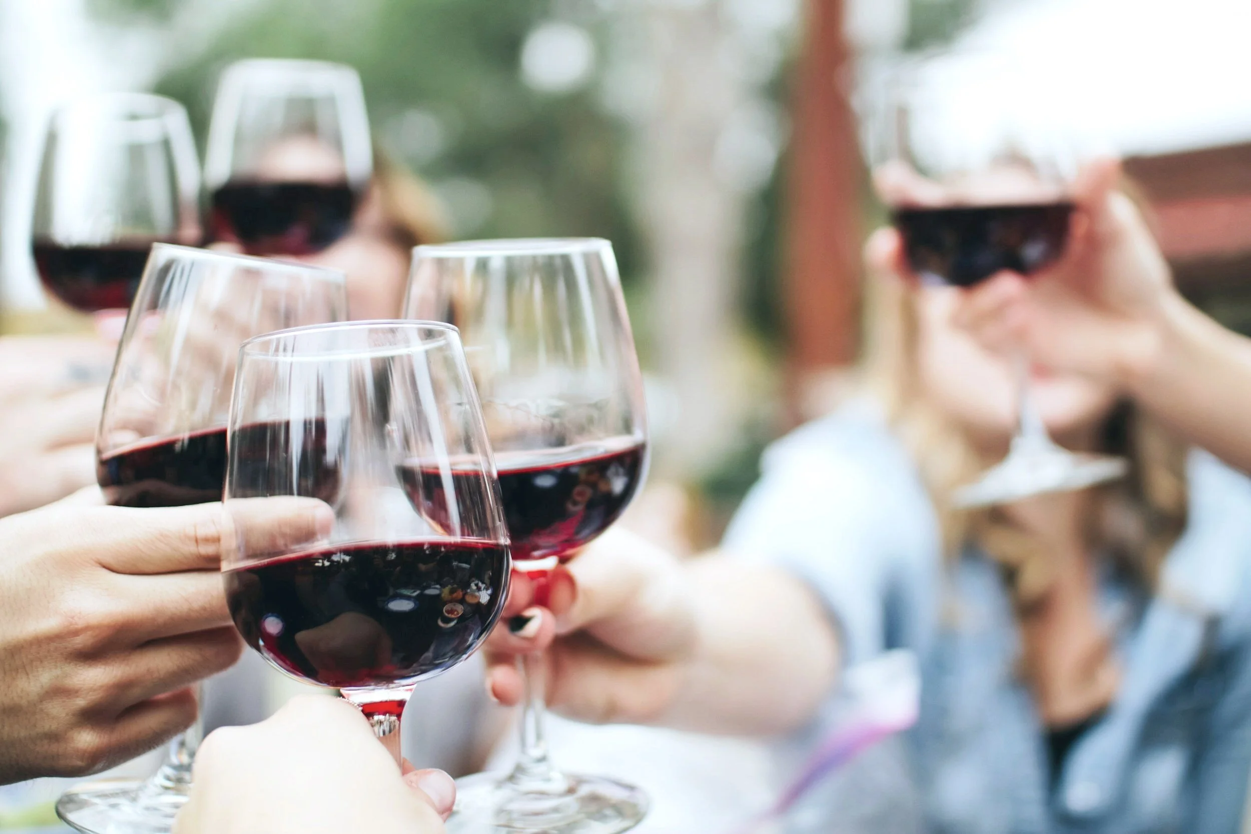People clinking glasses of red wine in a toast outdoors during daytime.
