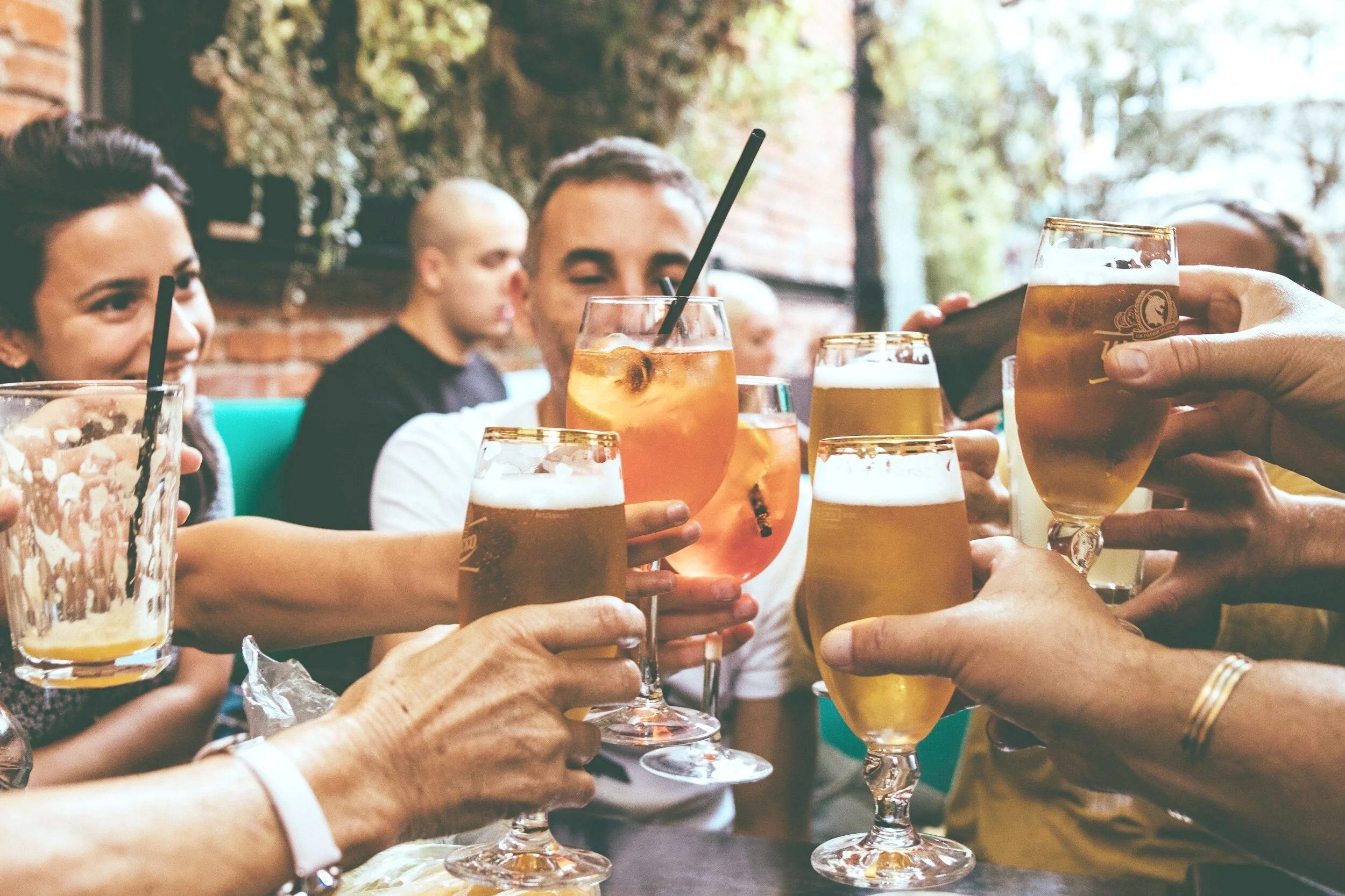 People enjoying drinks at a social gathering in a restaurant or bar, clinking glasses of beer and cocktails.