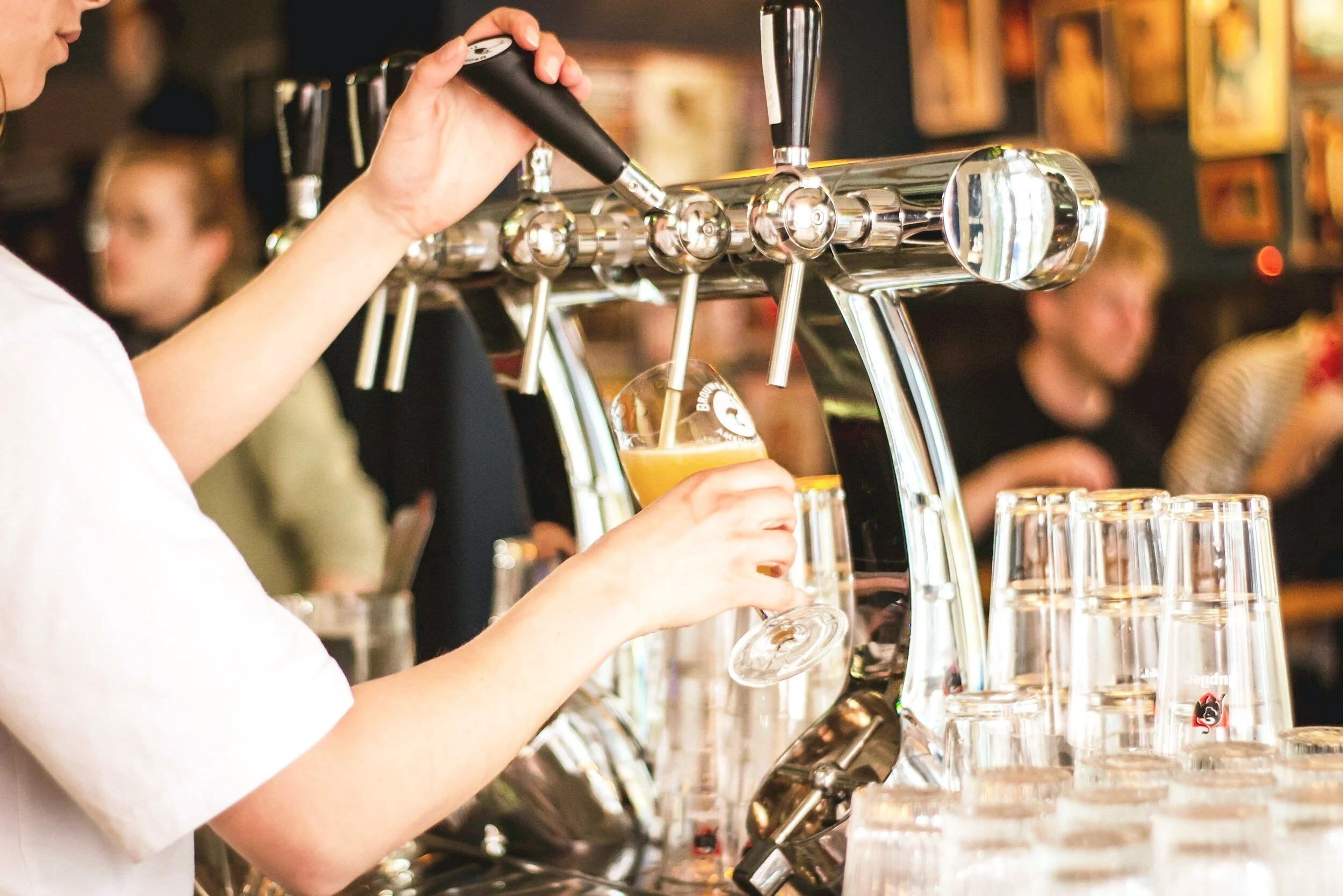 A person operating a draft beer tap dispenser at a bar, filling a glass with beer.