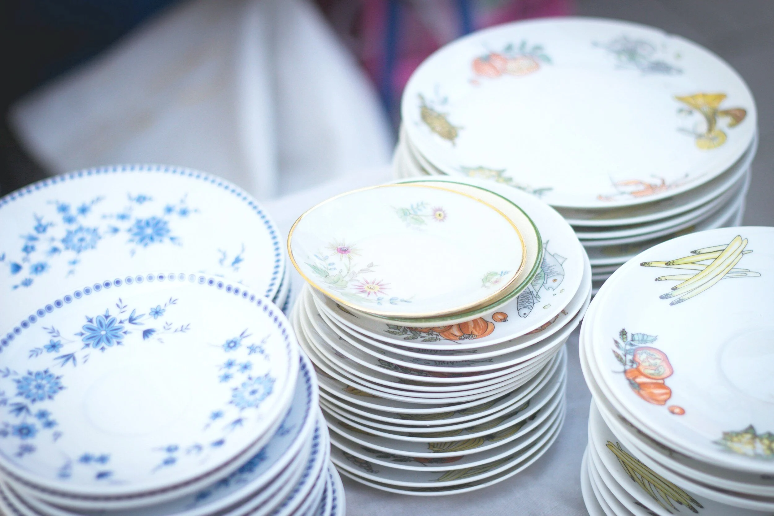 Multiple stacks of decorative ceramic plates with floral and patterned designs, some featuring images of animals and other motifs.