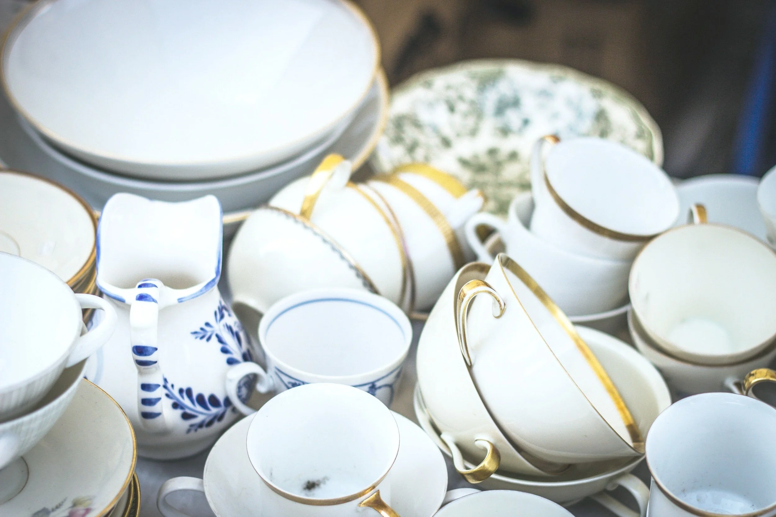 A collection of various white porcelain teacups and bowls with gold and blue decorative patterns stacked together.