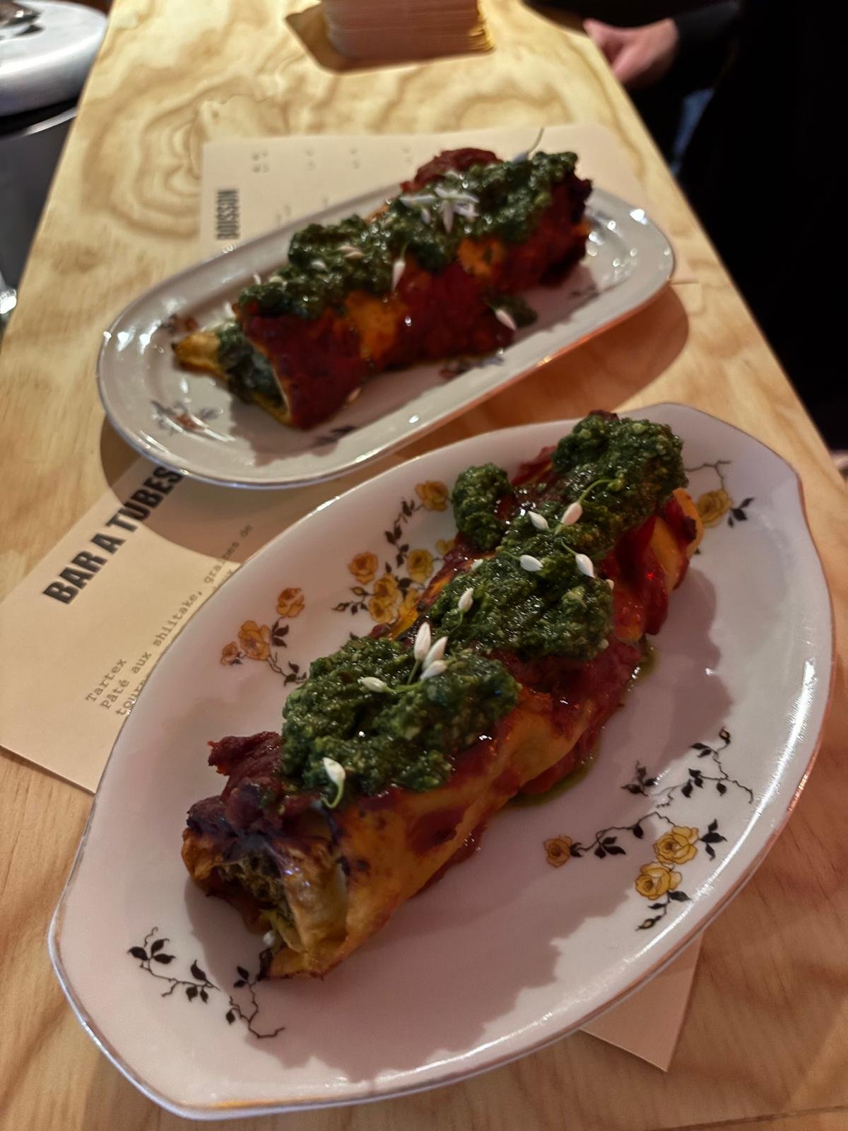 Deux plats de rouleaux de printemps garnis de légumes verts, servis sur des assiettes décoratives, avec une sauces verte en topping, dans un restaurant.