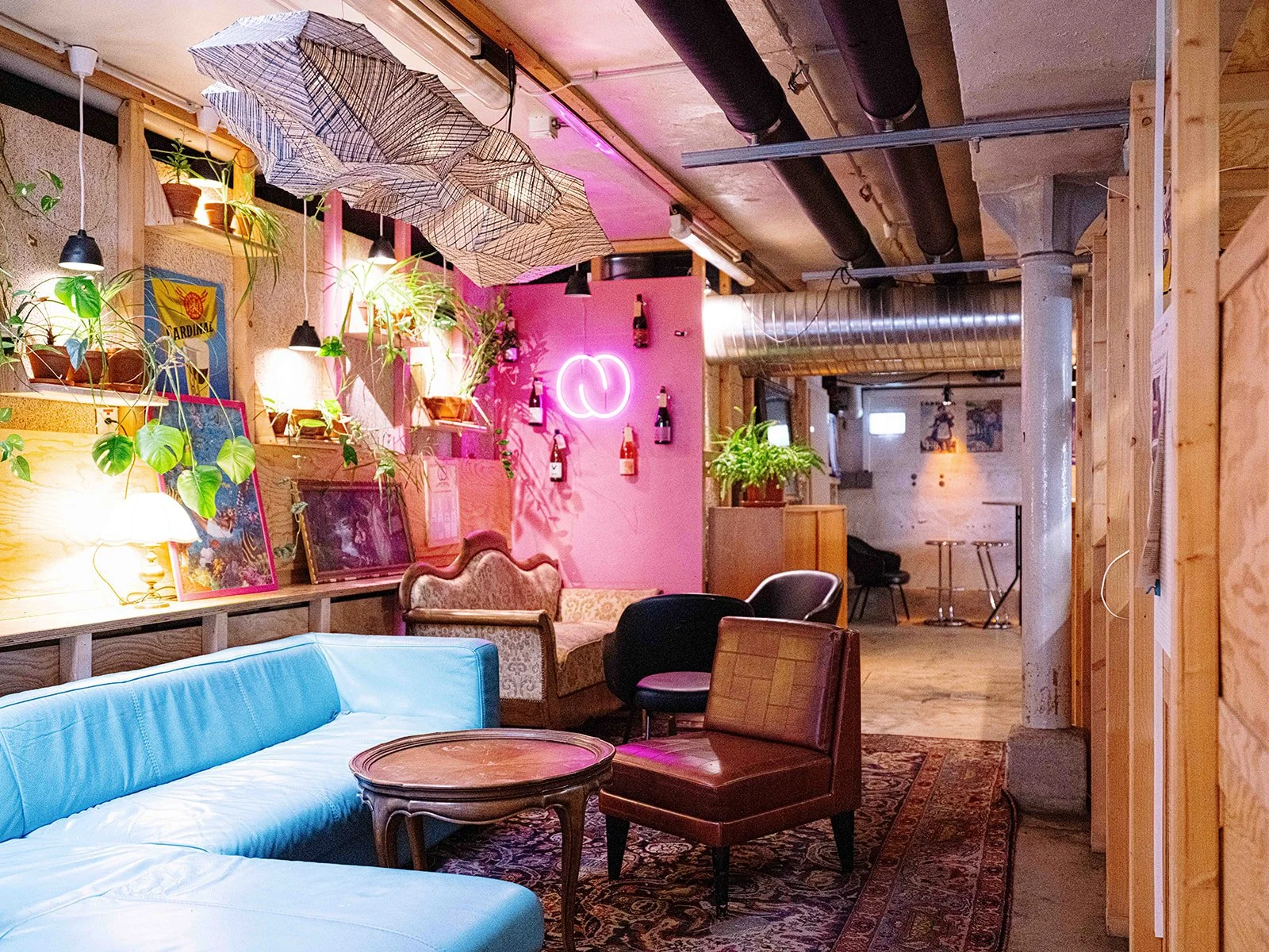 Intérieur d'un café ou salon avec des meubles vintage, des plantes, des lampes et décorations lumineuses, notamment un néon rose en forme de cercle.